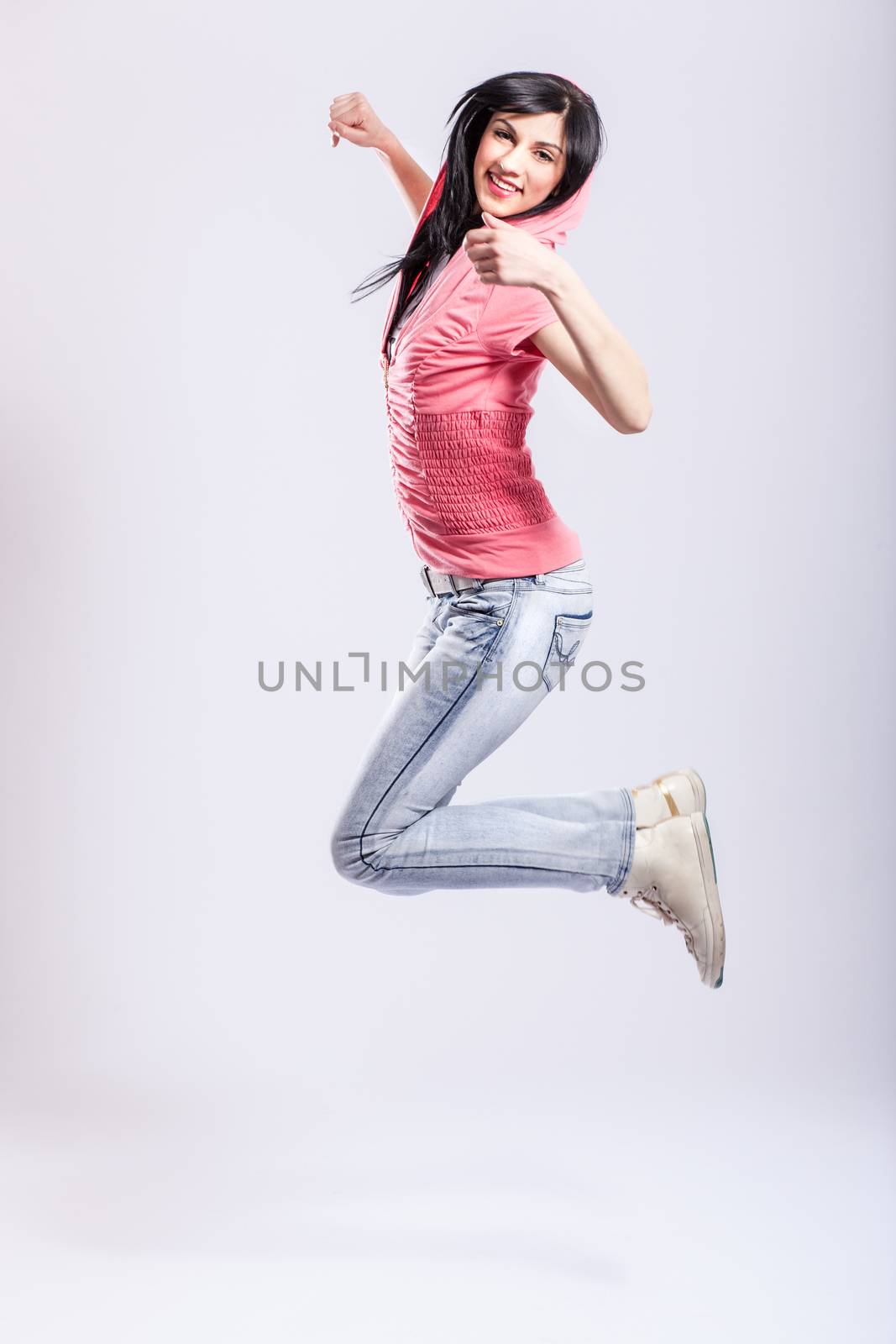 attractive young girl jumping, wearing pink hoodie and jeans