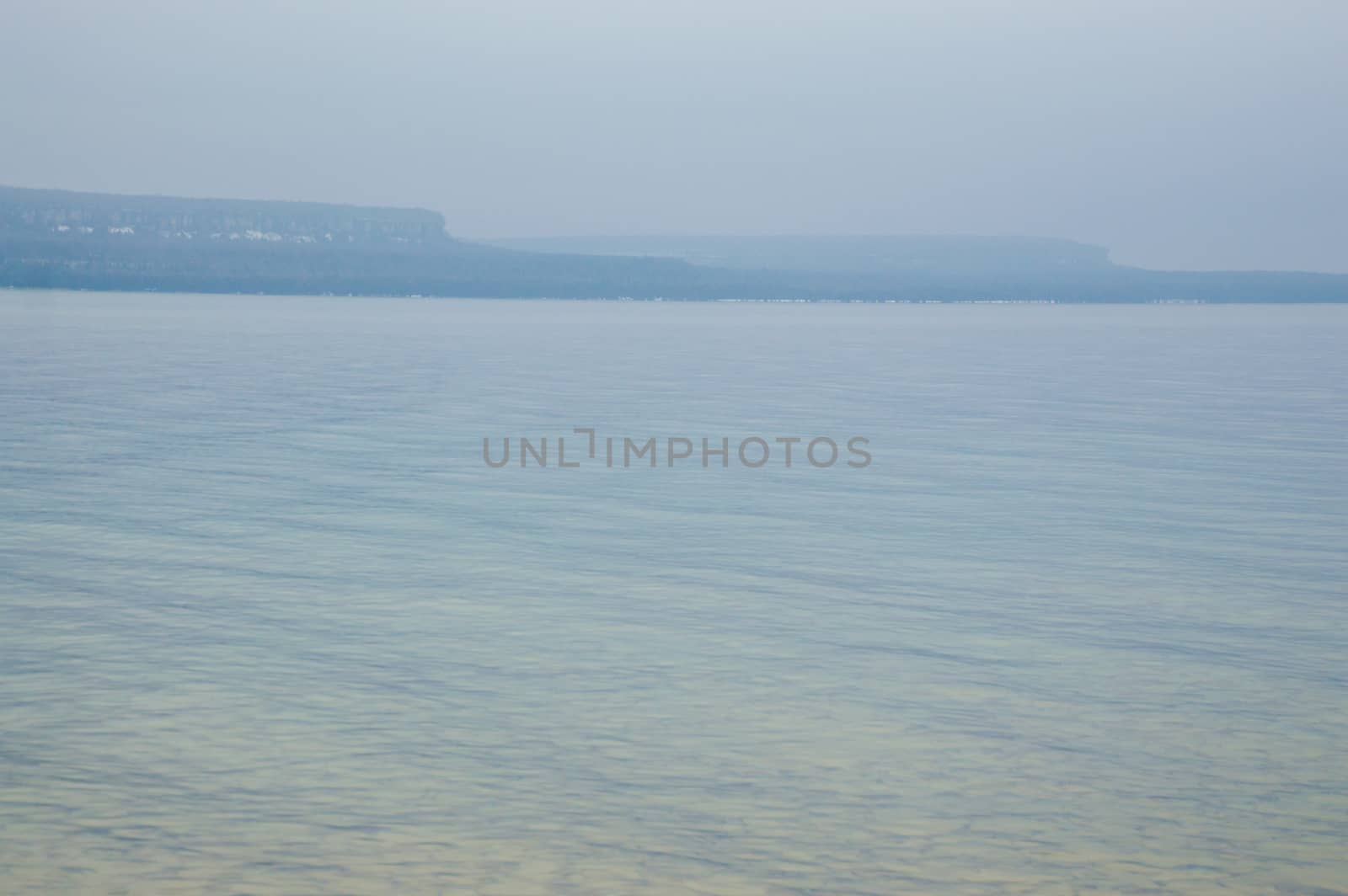 Image has the limestone escarpment cliffs in the distance with reflected yellow and blue ripples and waves in the crystal clear lake