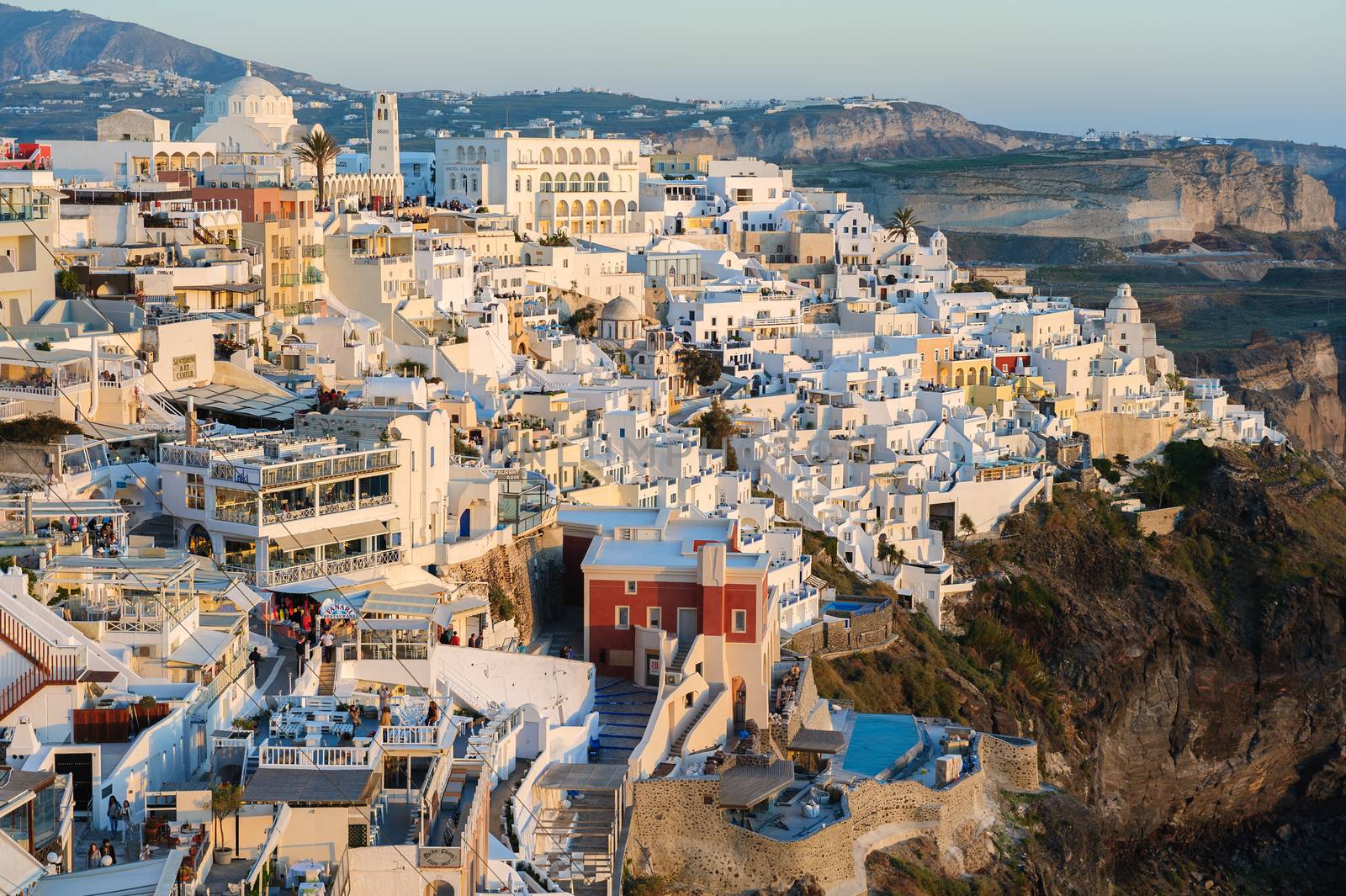 Fira, Santorini island, Greece - April 2016: Illuminated Luxury balcony decks and patios with restaurants of Fira town at Santorini island, in warm rays of sunset. Santorini is one of most famous greek resorts situated in Aegean sea at old volcano's caldera.