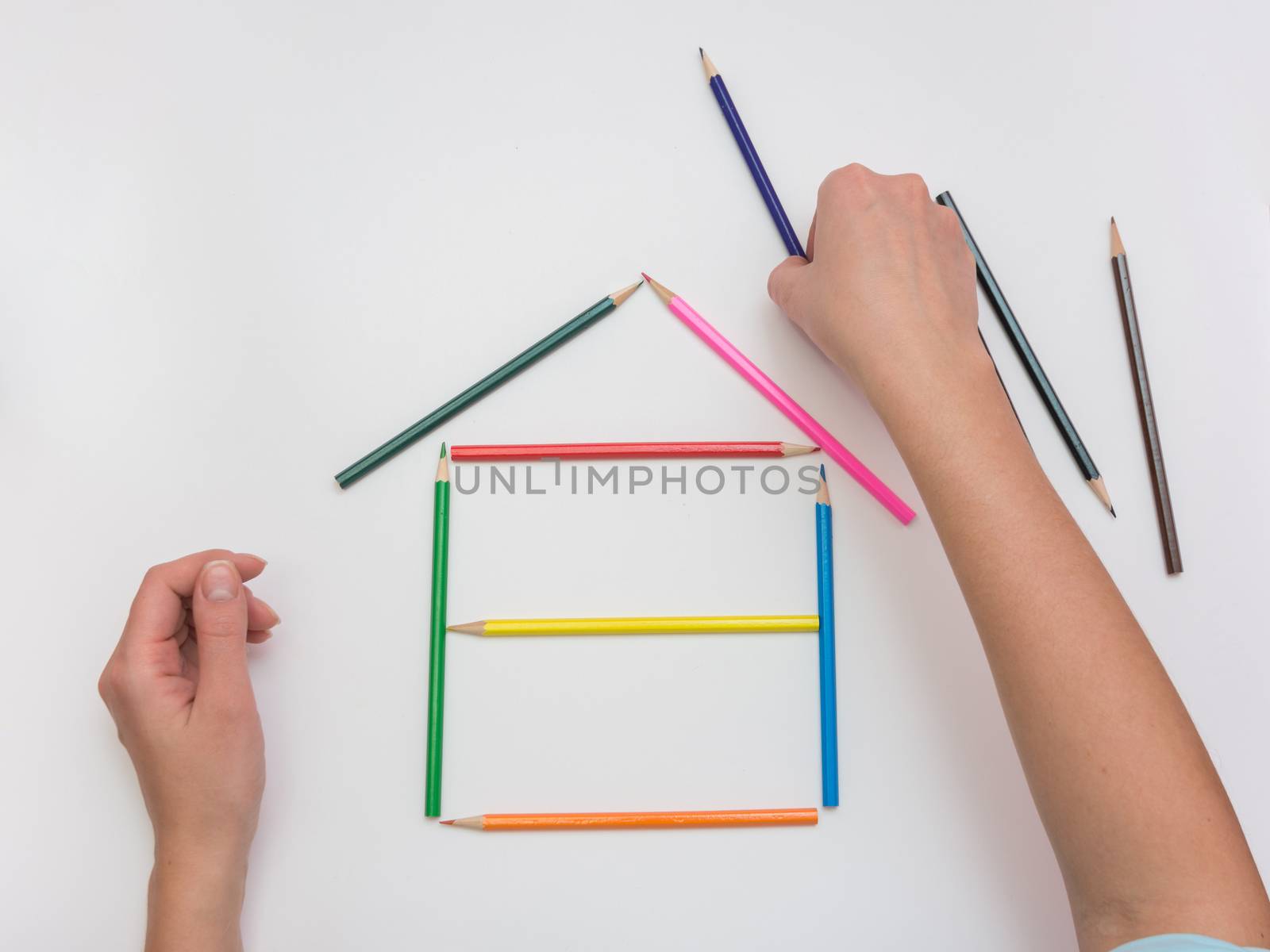 Women's hands are building a wooden house from pencils by Madhourse