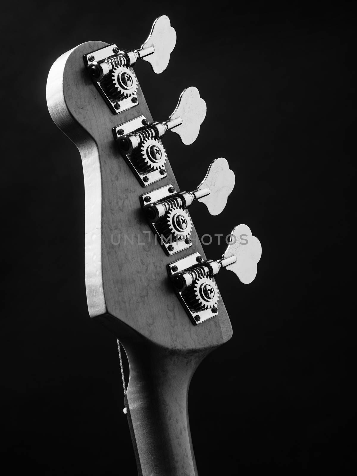 Black and white photo of a bass guitar headstock over black background.