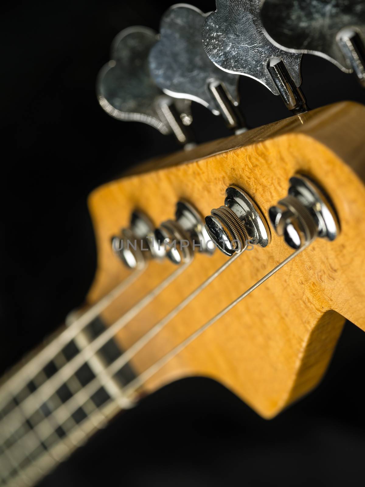 Photo of a bass guitar headstock over black background.