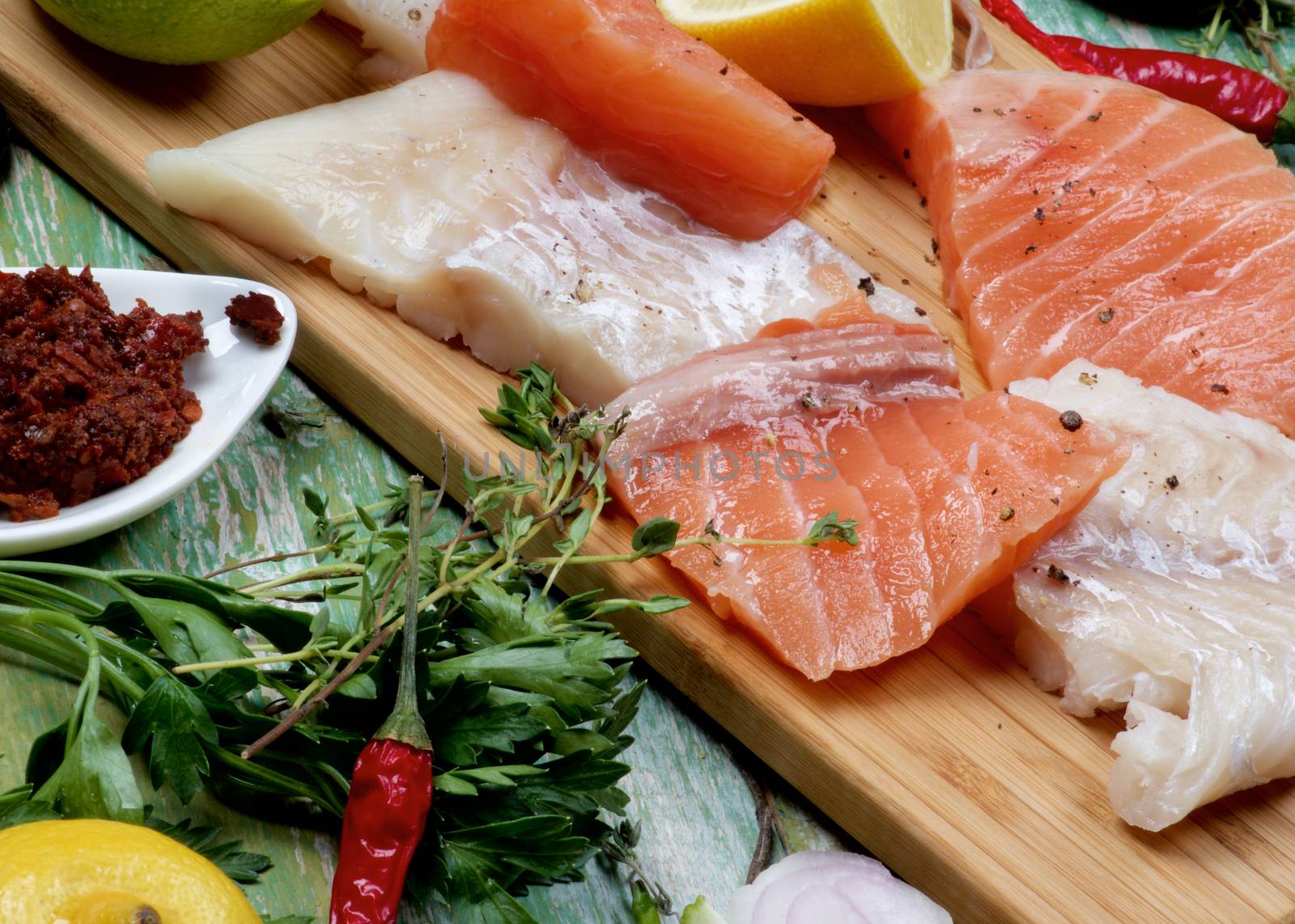 Concept of Seafood with Big Slices of Raw Fillet of Salmon and Cod, Greens, Spices and Lemon closeup on Cracked Wooden background