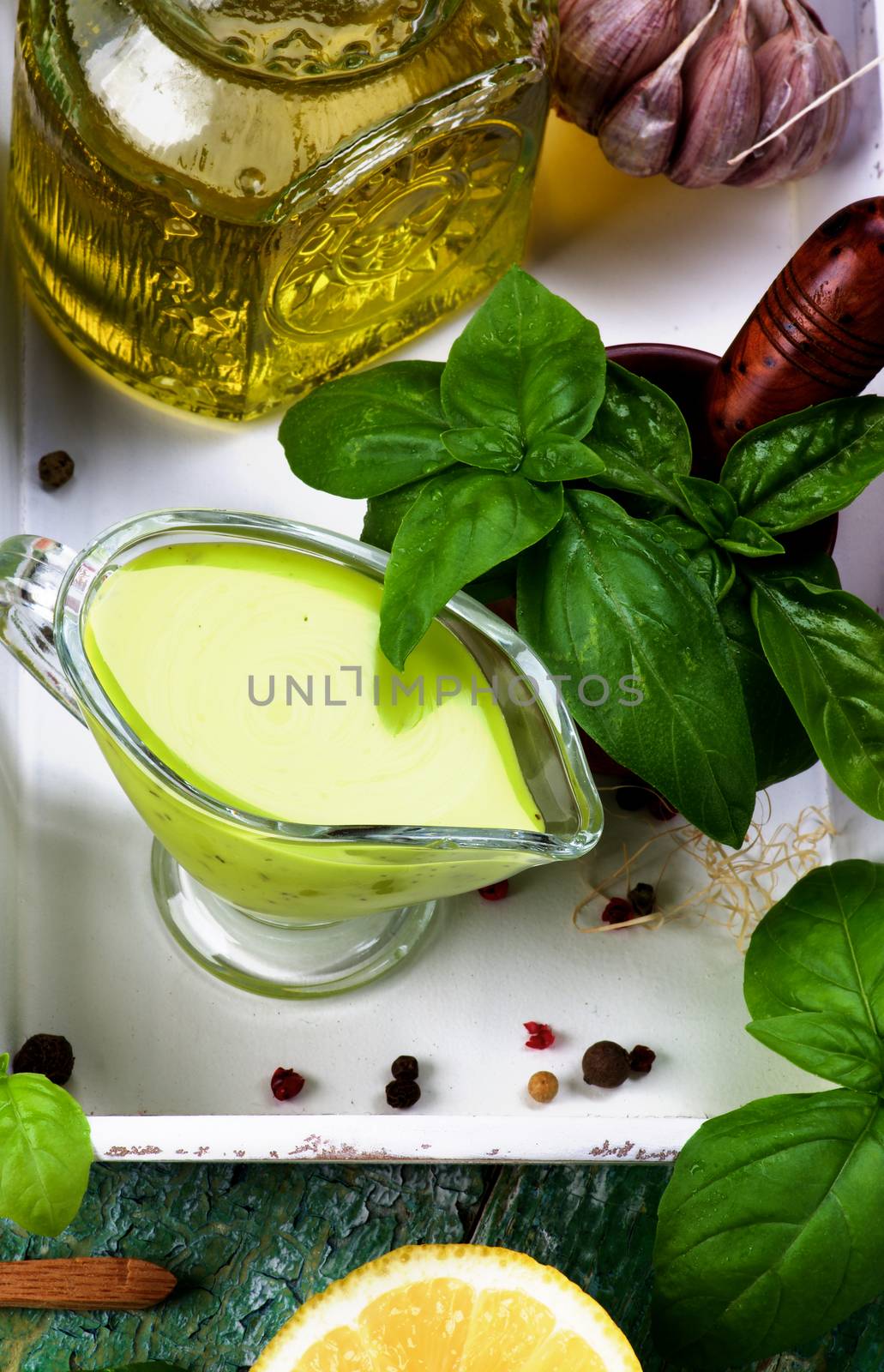 Freshly Made Creamy Pesto Sauce in Glass Gravy Boat with Fresh Basil Leafs, Raw Ingredients and Olive Oil in White Wooden Tray closeup. Top View