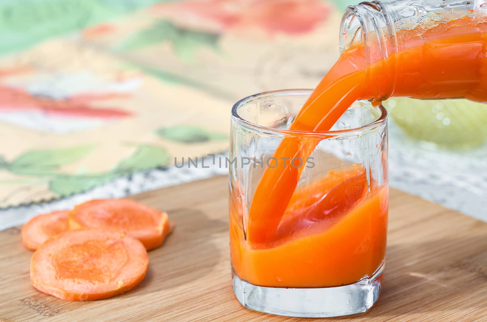 Fresh carrot juice is poured into a glass from the bottle. Selective focus. by Gaina