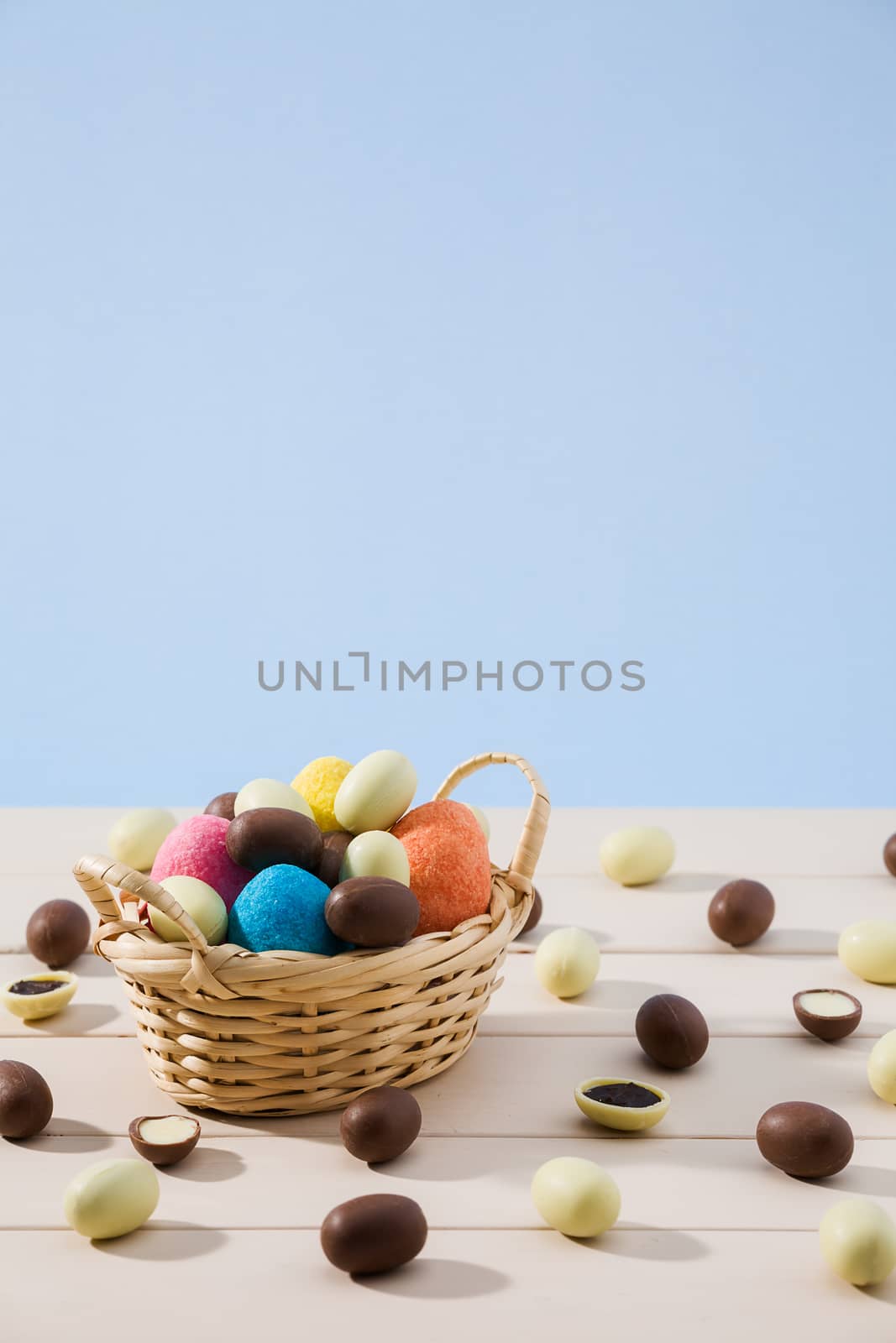 Easter chocolate eggs in a small basket and some small eggs over a white table with blue background