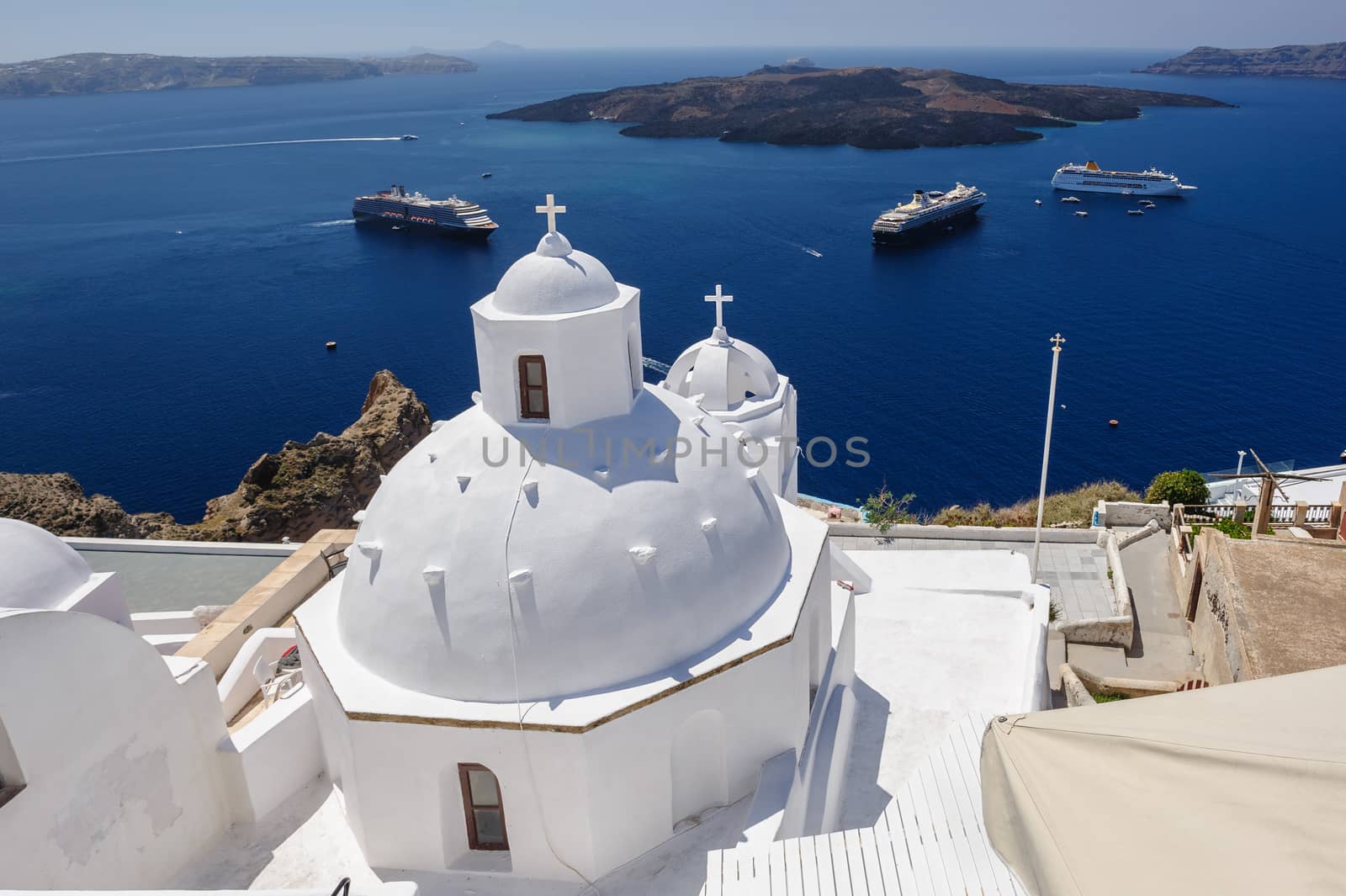 White orthodox church bell tower and sea with ships at background. Fira, Santorini Greece. Copyspace