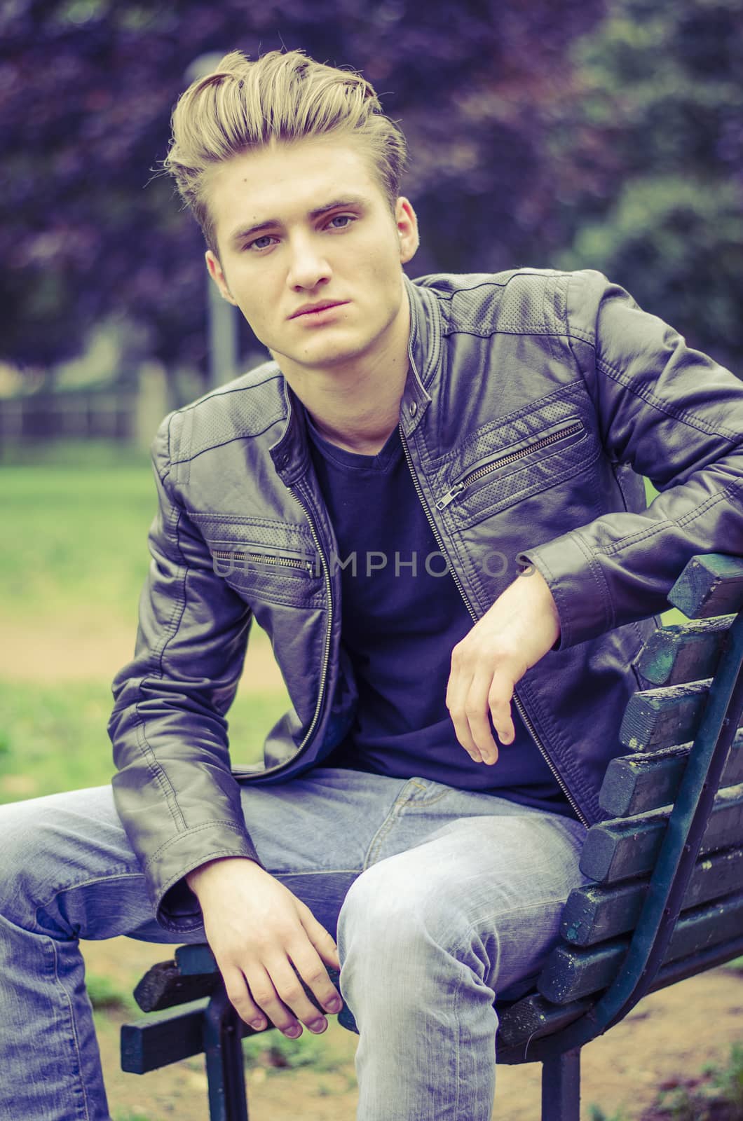 Handsome blond young man sitting on park bench by artofphoto