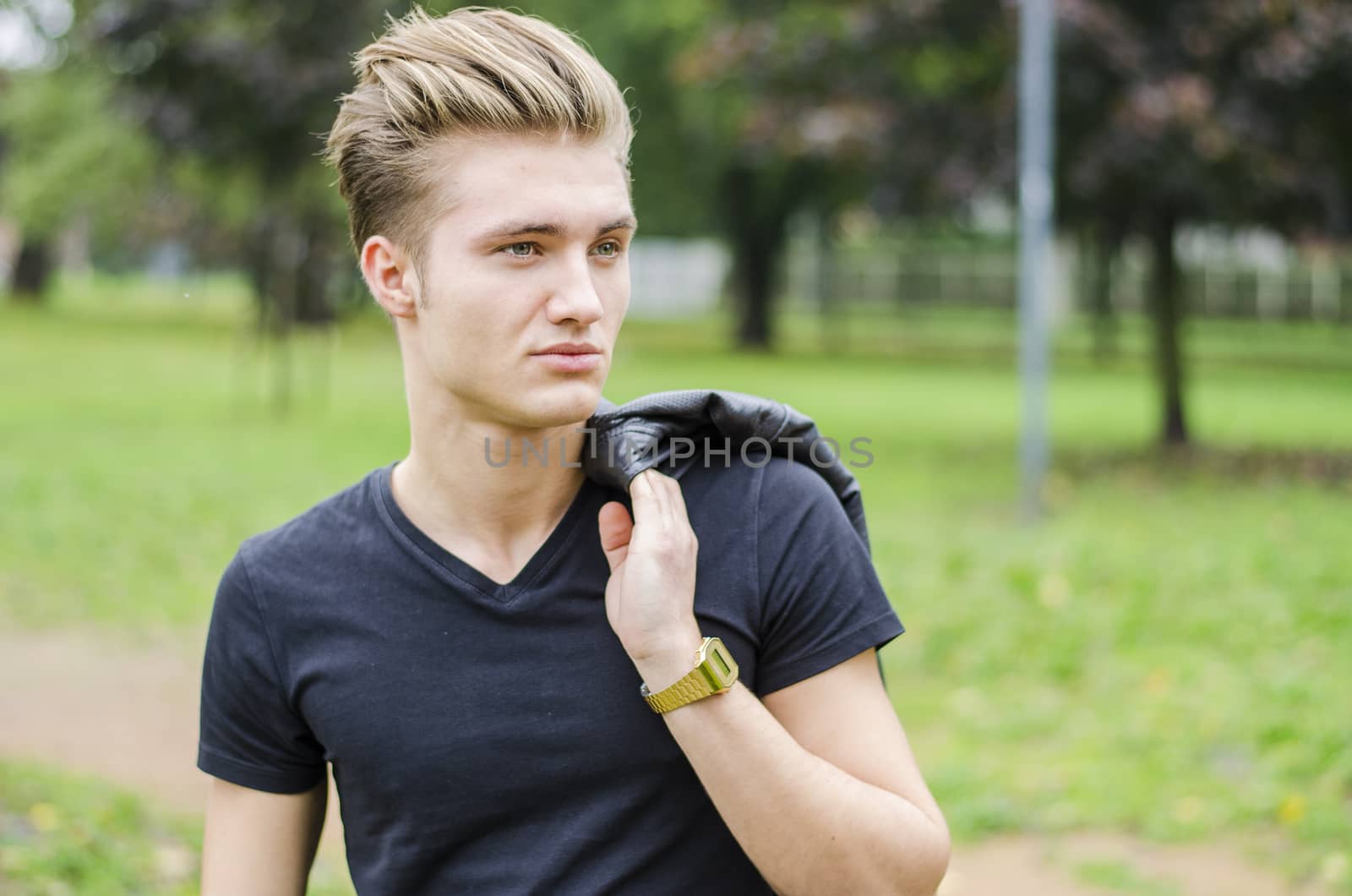 Attractive blond young man outdoors in a park, smiling