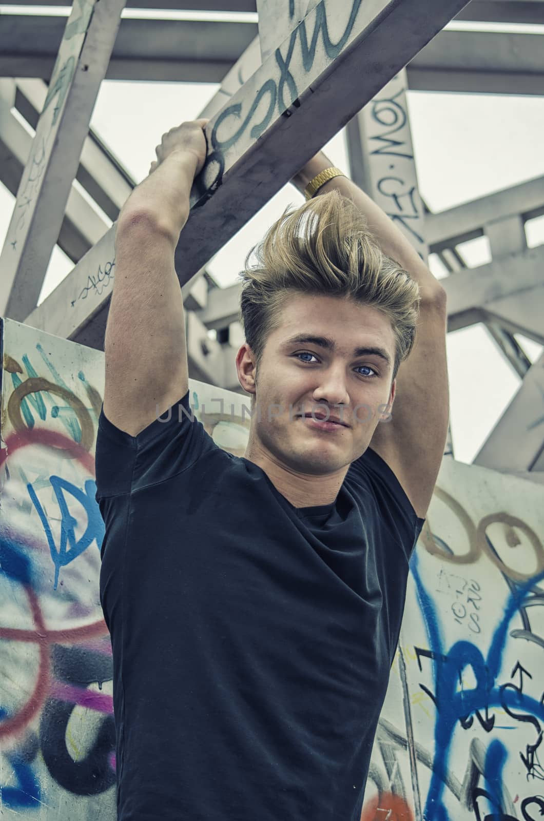 Attractive blue eyed, blond young man in black t-shirt hanging from concrete structure