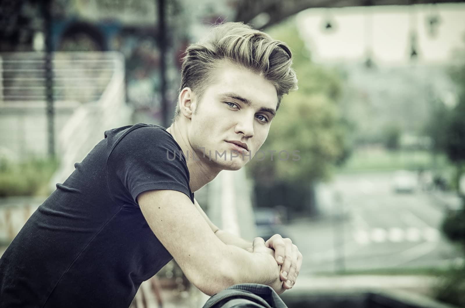 Profile shot of attractive blond young man in city, looking at camera, outdoor