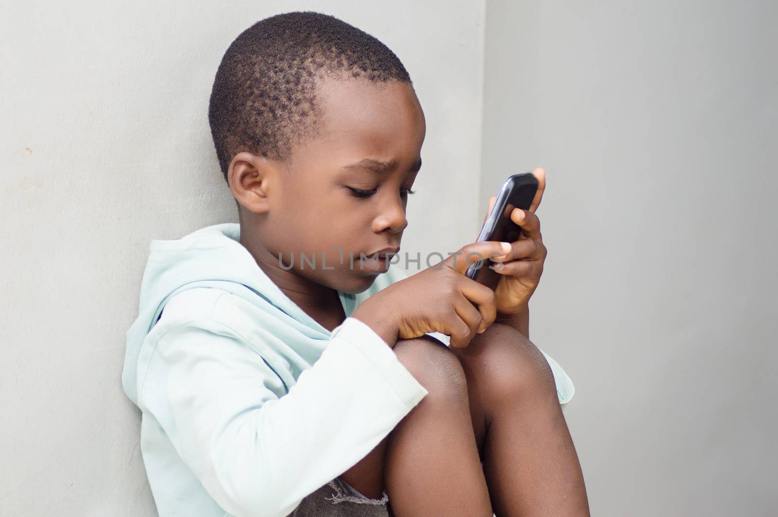a child sitting against the wall manipulating a mobile phone with curiosity.