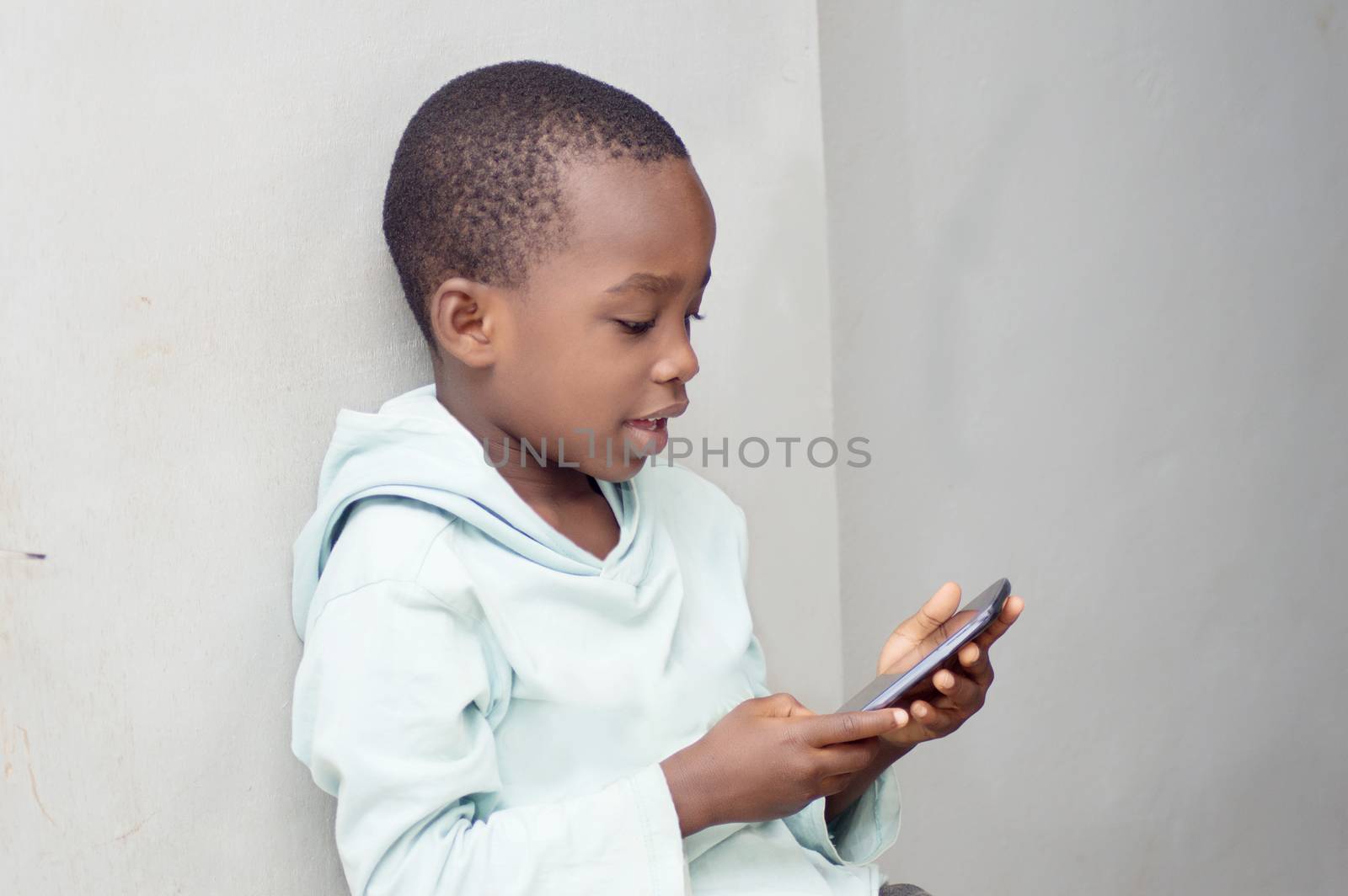 This little boy sitting against the wall manipulates a mobile phone with emotion.