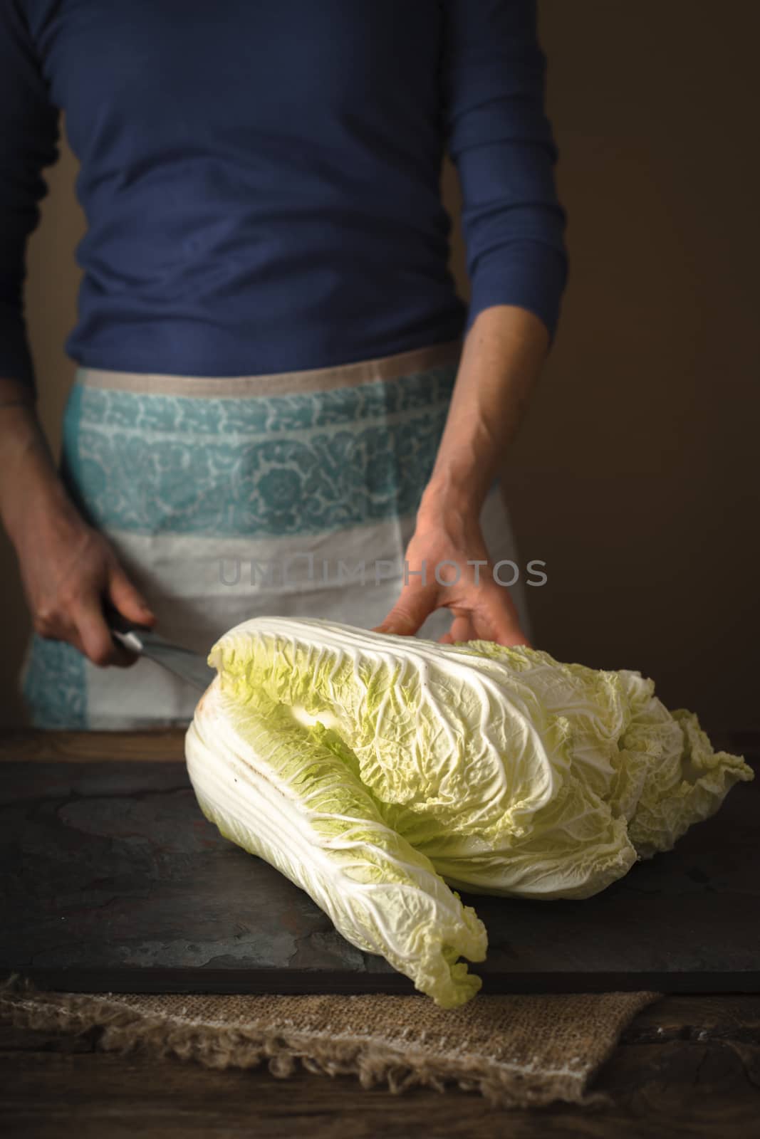 Woman cuts Chinese cabbage on a gray slate vertical