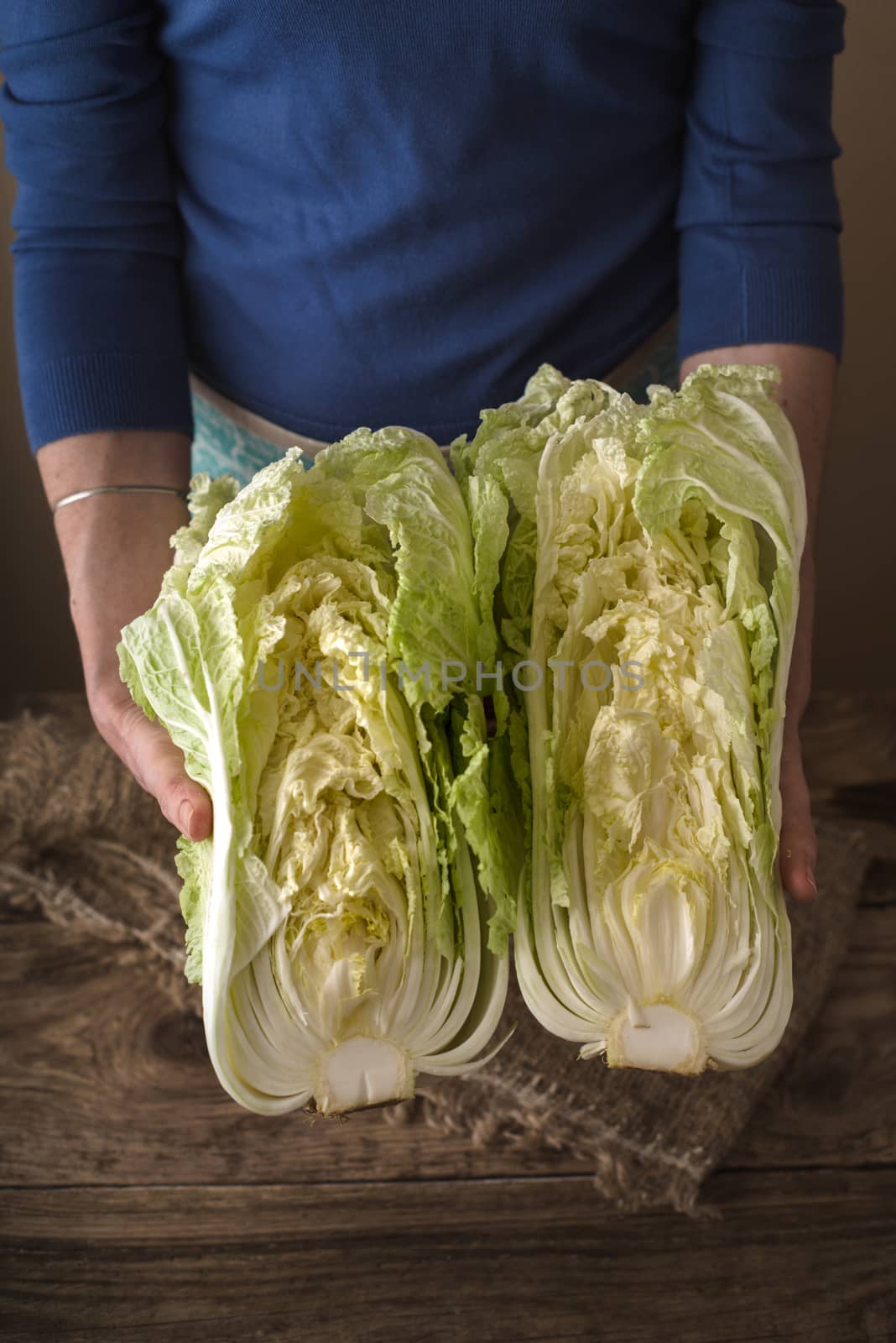 Woman holding two halves of the Chinese cabbage on the table by Deniskarpenkov