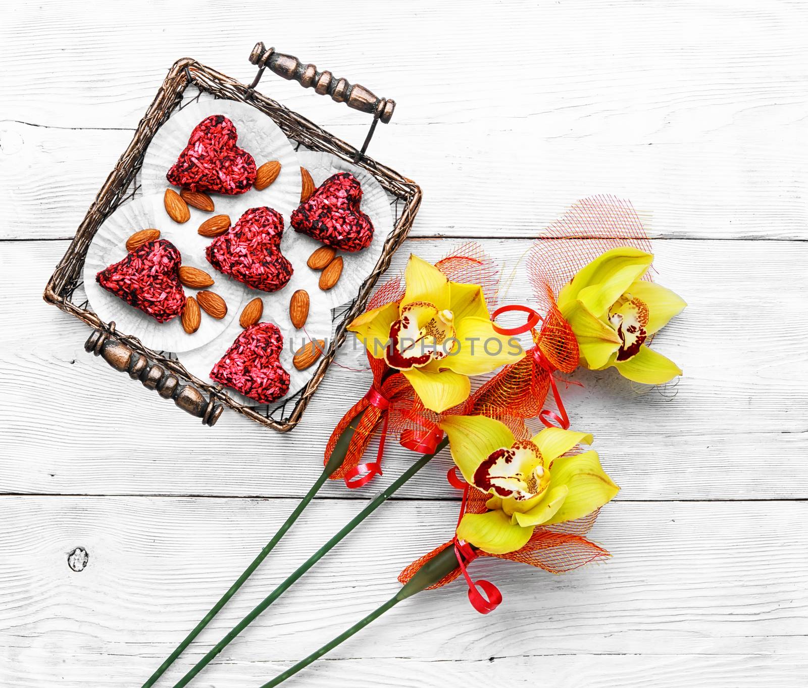 Stylish metal basket with candies in shape of heart and bouquet of orchids