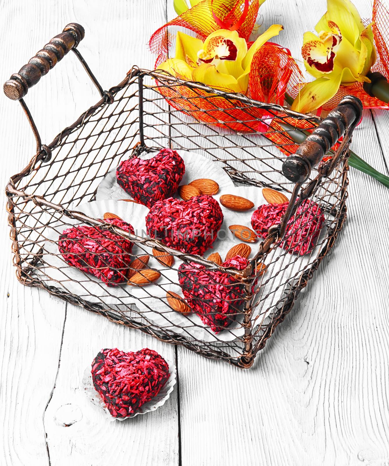 Stylish metal basket with candies in shape of heart and bouquet of orchids