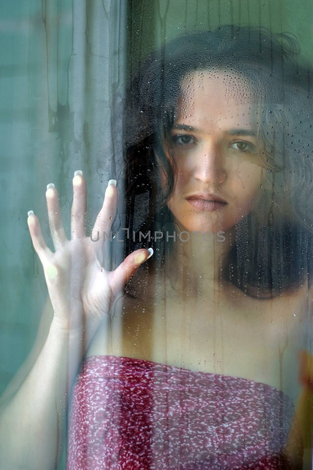 Woman with sad smile behind a wet window