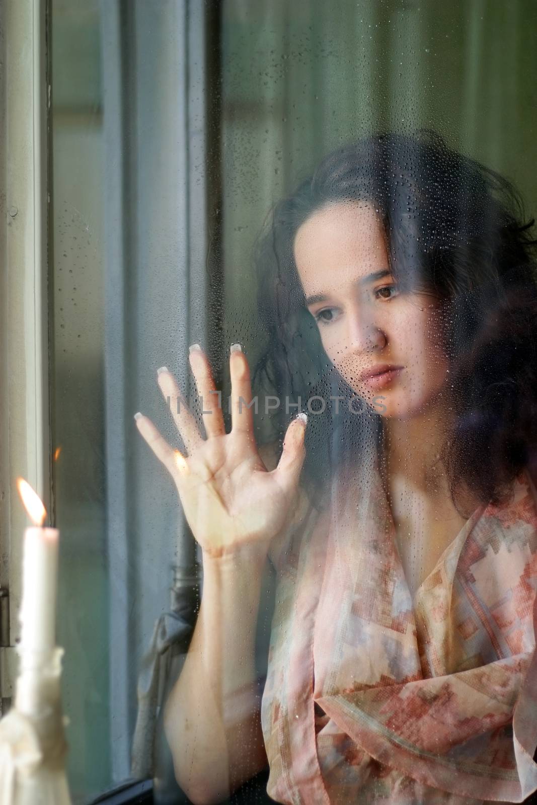 Woman with sad smile behind a wet window