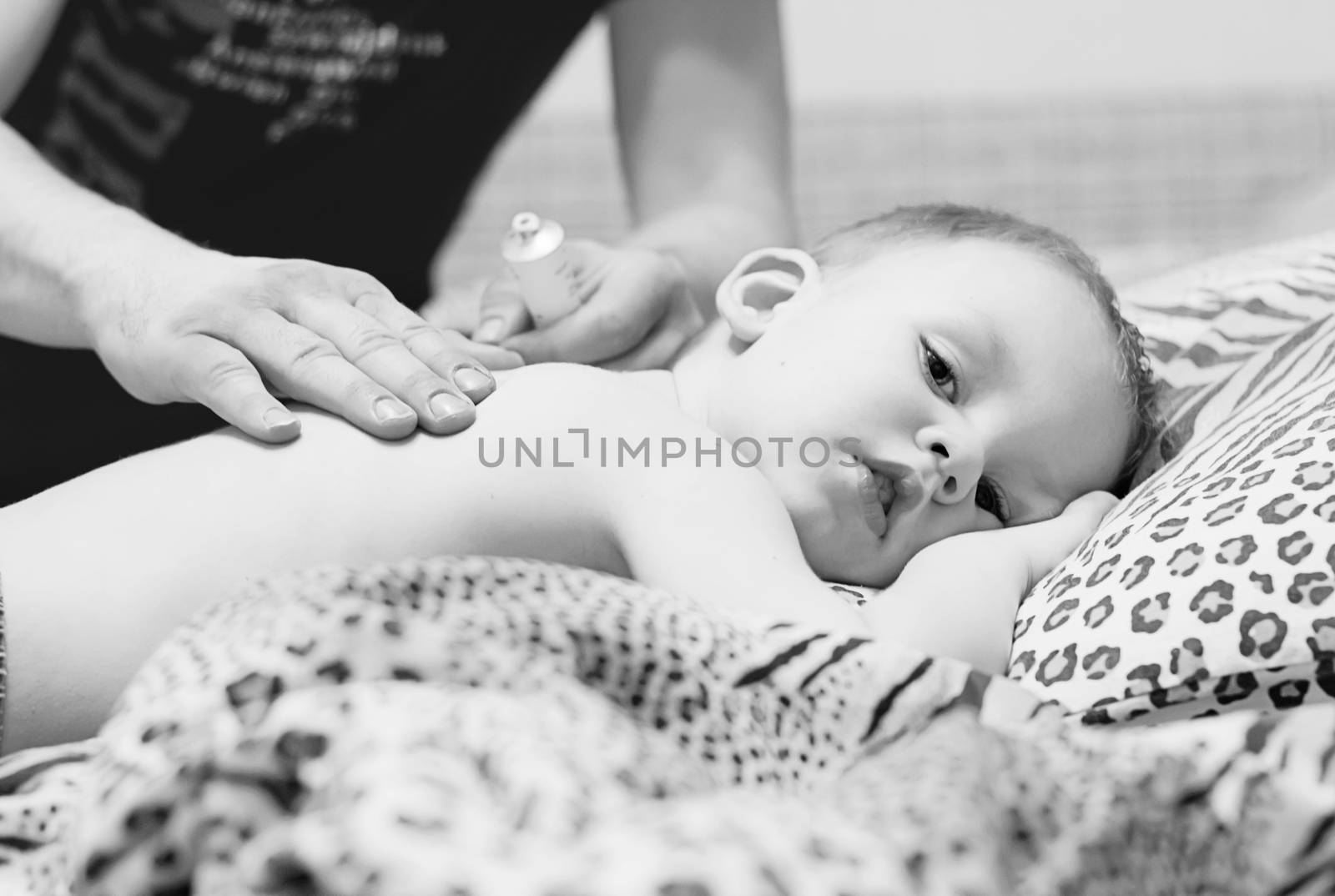 Father rubs the back of a sick child with ointment. Men's hands do massage to the child. Black and white photography