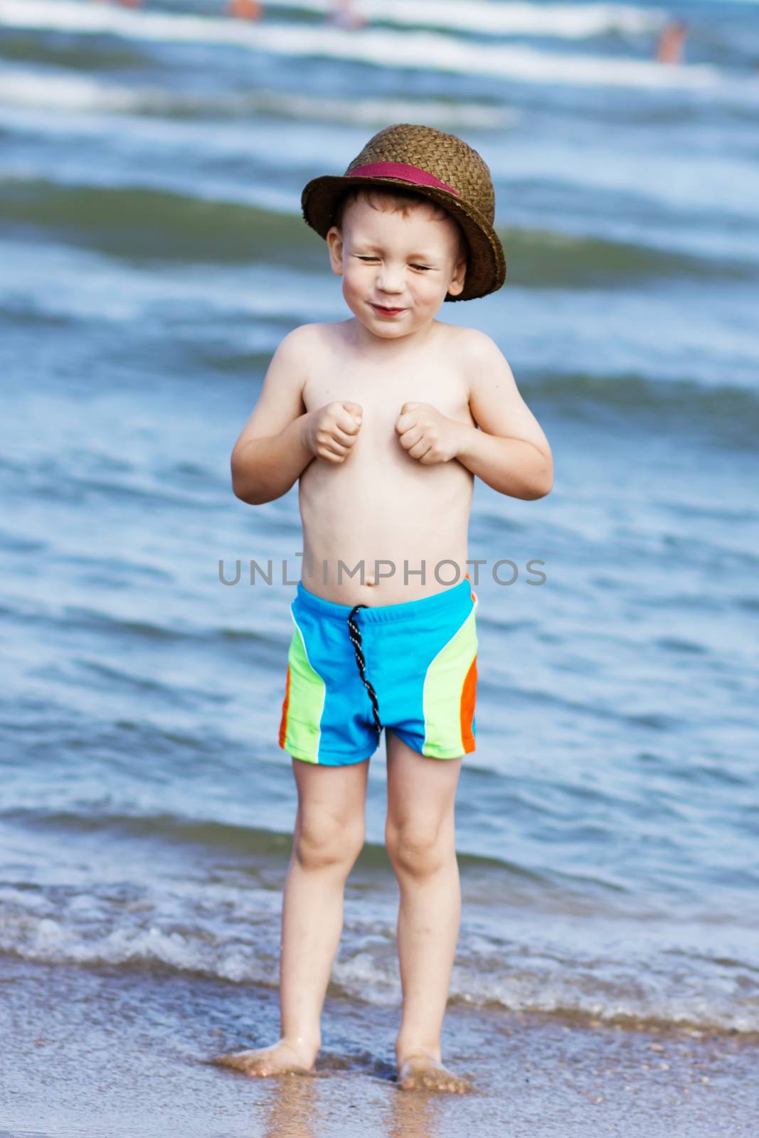 little boy standing standing on the beach and laughing by natazhekova