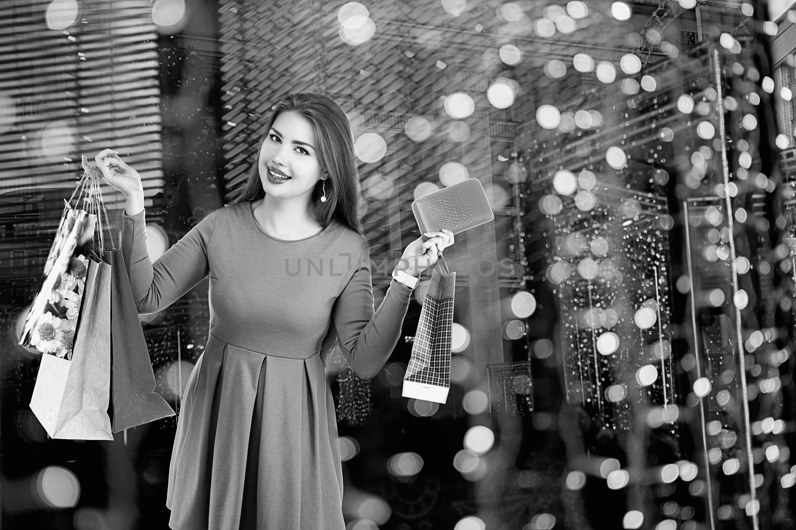 Beautiful happy girl posing with shopping bags against bokeh background. Black and white photography