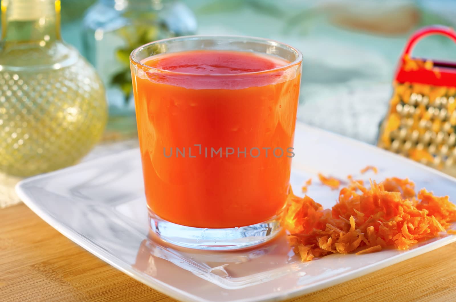 Carrot juice in a glass on a plate, utensils and a bit of grated carrots. Selective focus.