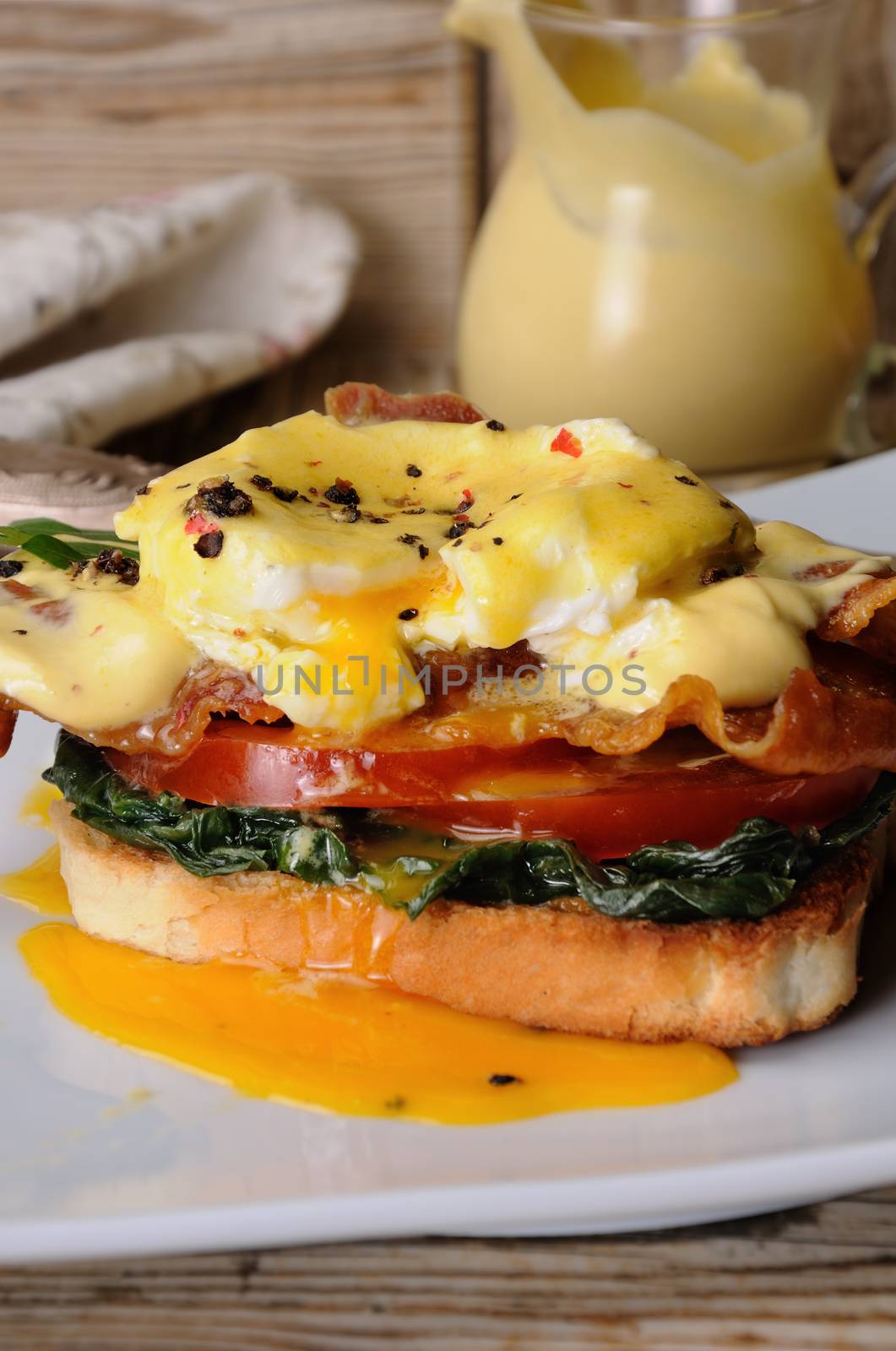 Eggs Benedict with tomato, slices of bacon, spinach under hollandaise sauce on toast
