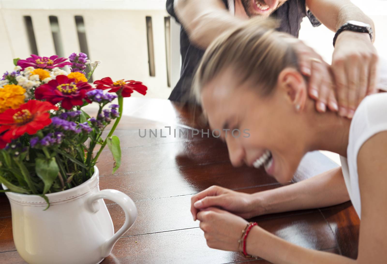 Motion blurred figures of playful young couple indoors. The man is squeezing the woman s neck. Female is laughing.