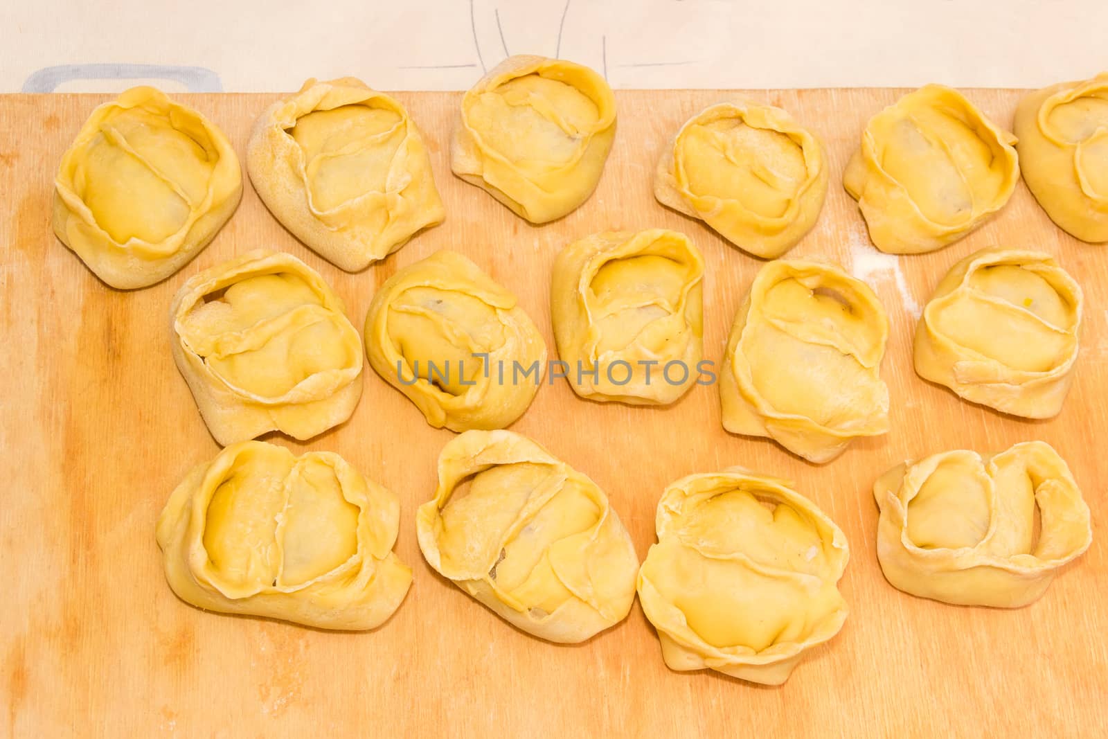 Uncooked manti (dumplings, meat dumplings) on a wooden cutting board during cooking 
