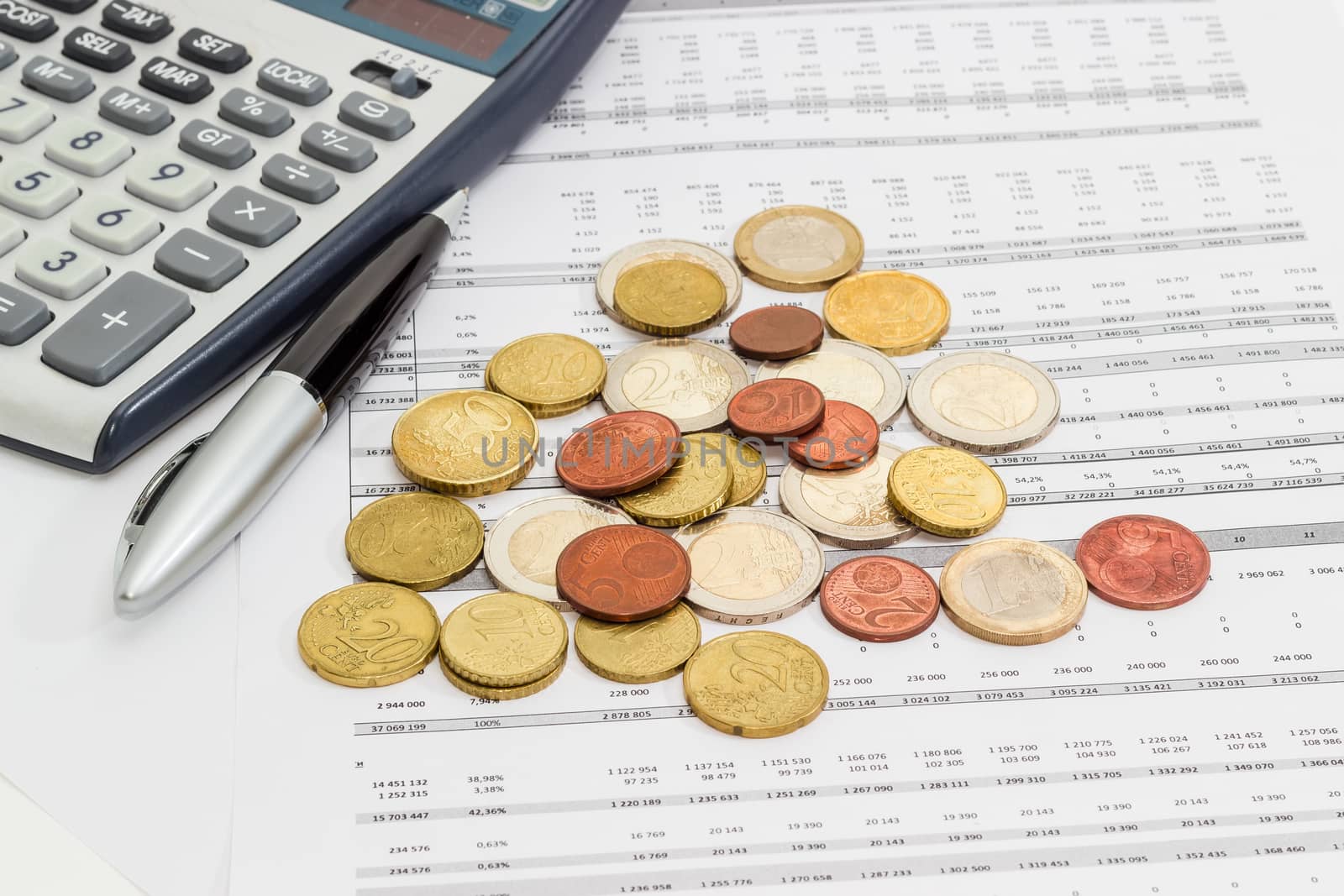 Several euro coins from 1 cents to 2 euro scattered on the printed table with data, pen and fragment of a calculator 
