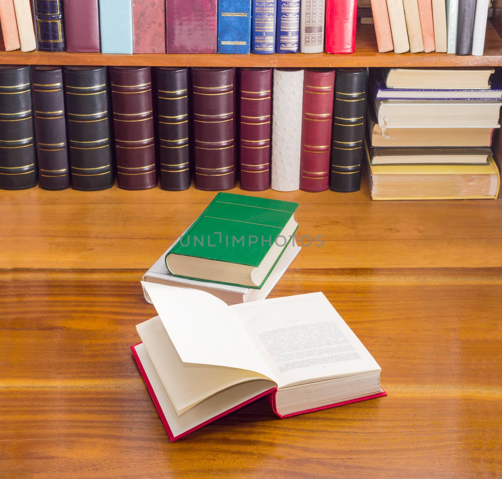 Open book, stack of two books different formats and cover design on a wooden table against the background of shelf with books
