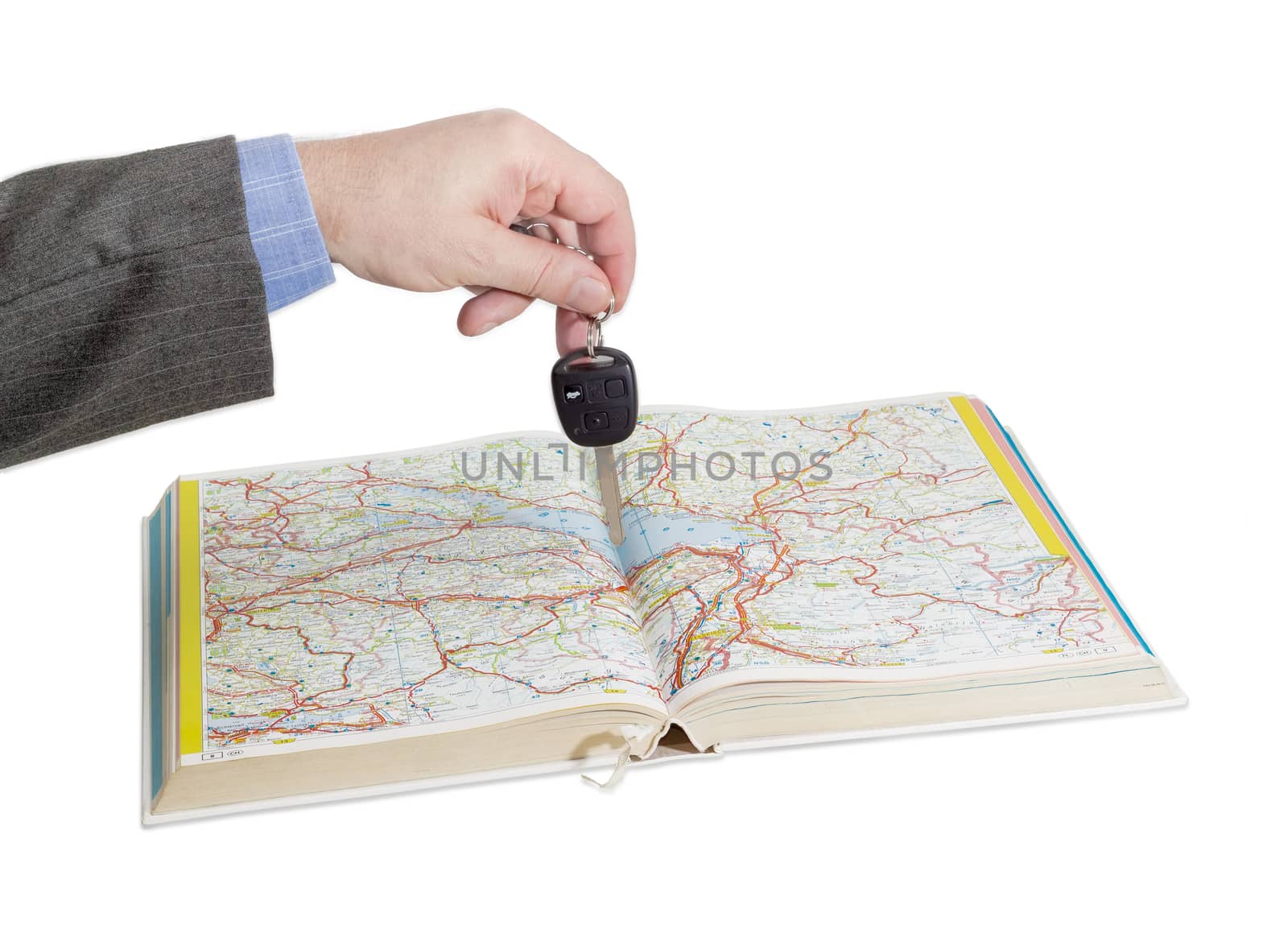 Male hand with car keys over an open old road atlas on a light background
