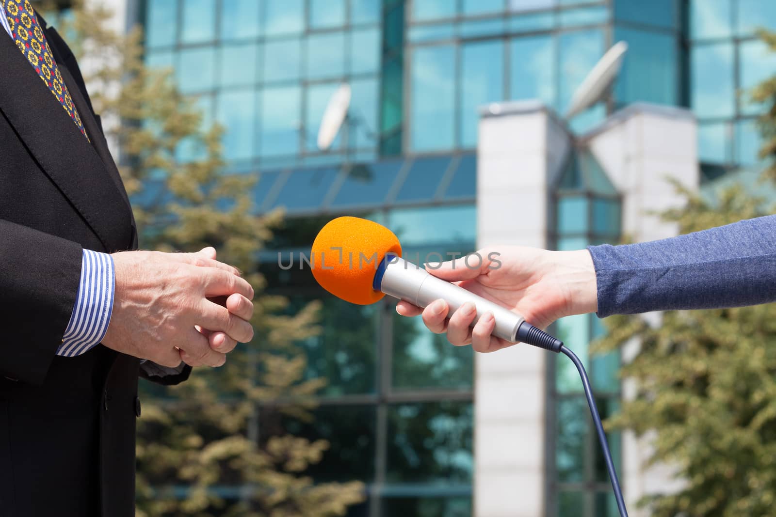 Reporter interviewing businessman, corporate building in background by wellphoto