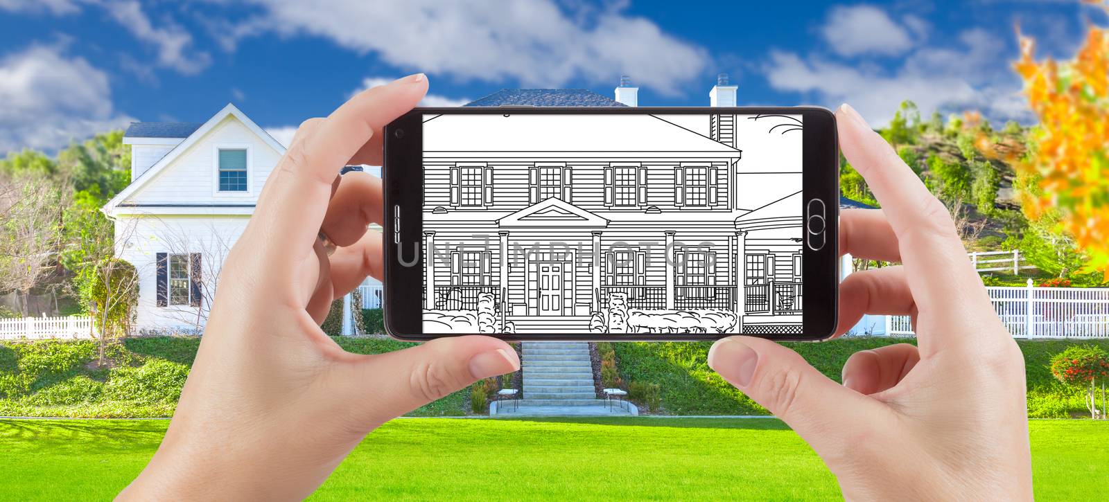 Hands Holding Smart Phone Displaying Drawing of Custom Home Photo Behind.