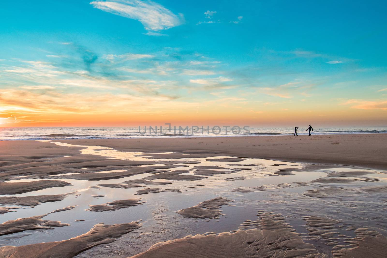 A father and teenager son playing racket in the beach during a winter evening right before sunset