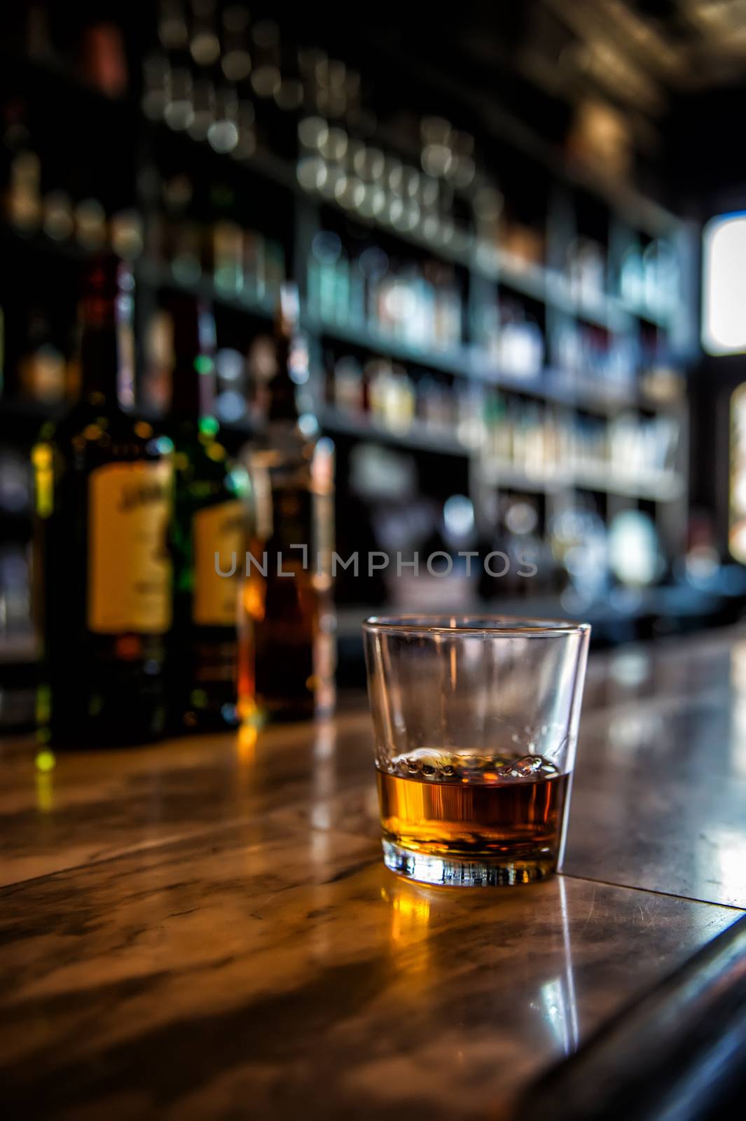 Image of a glass of whiskey on a bar with blurred background