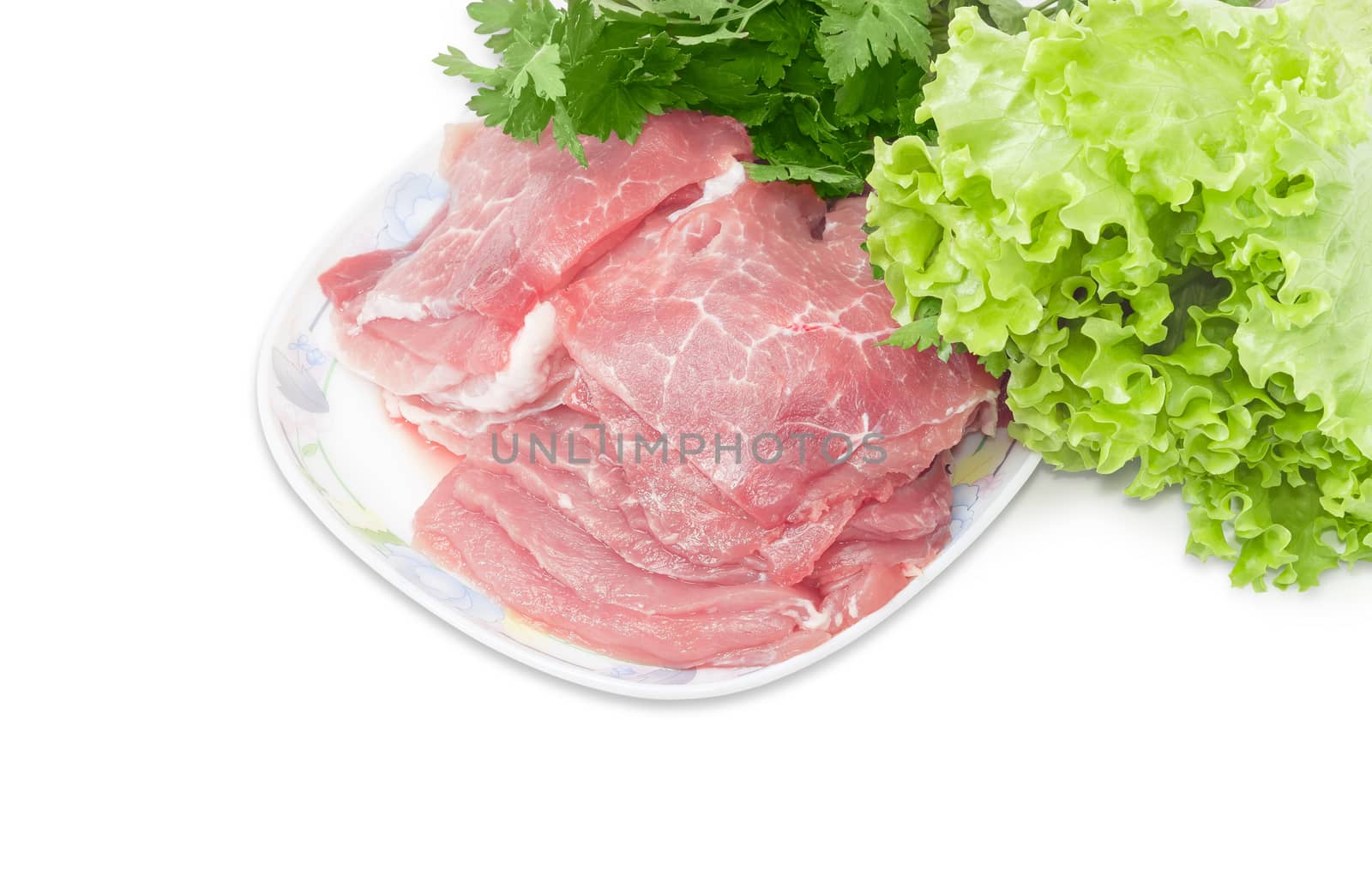 Sliced fresh chilled pork on a dish closeup against the background of bunch of parsley and lettuce on a light background 
