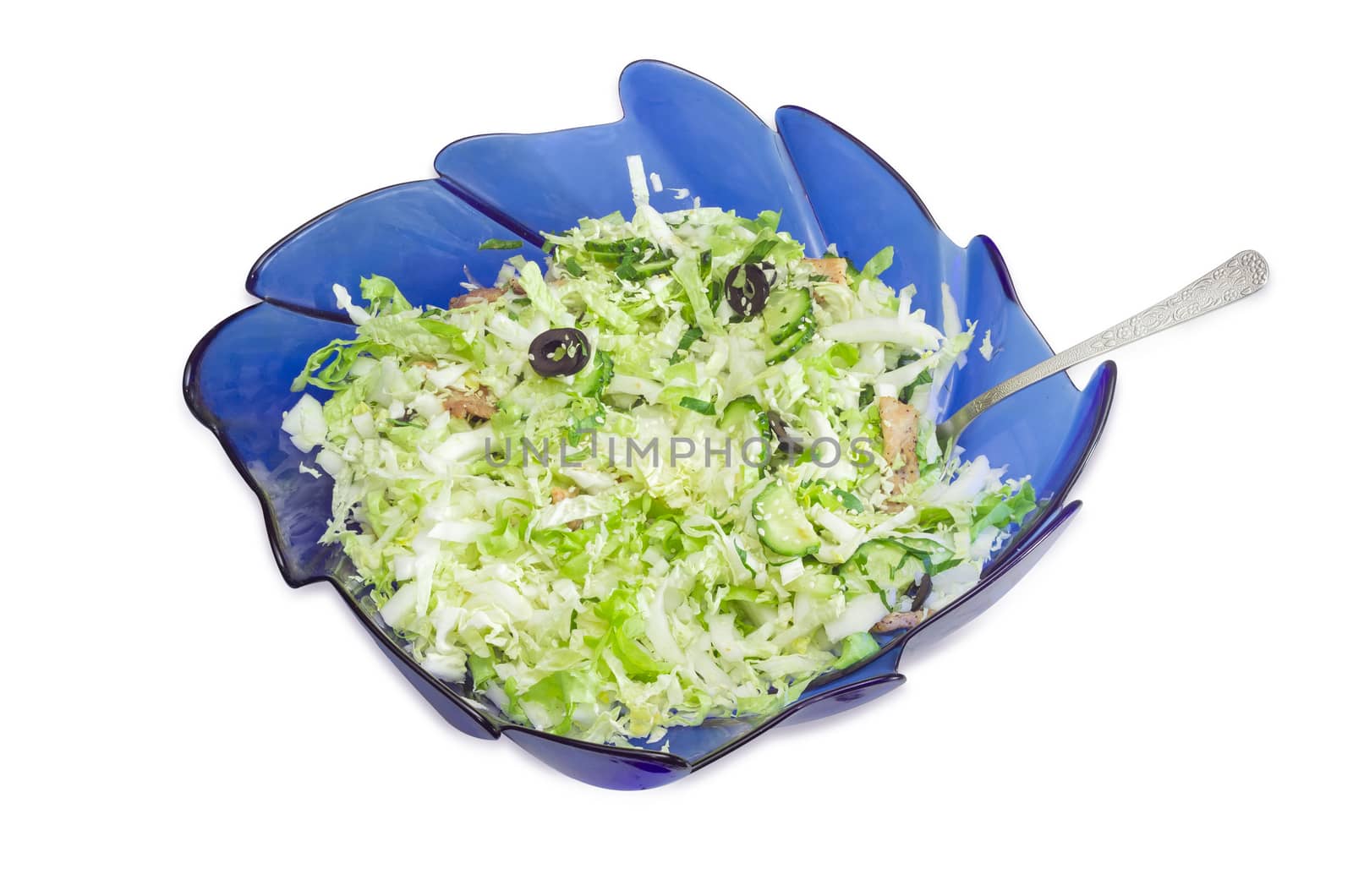 Vegetable salad made with napa cabbage, cucumbers, other vegetables, meat and olives in blue glass salad bowl on a light background
