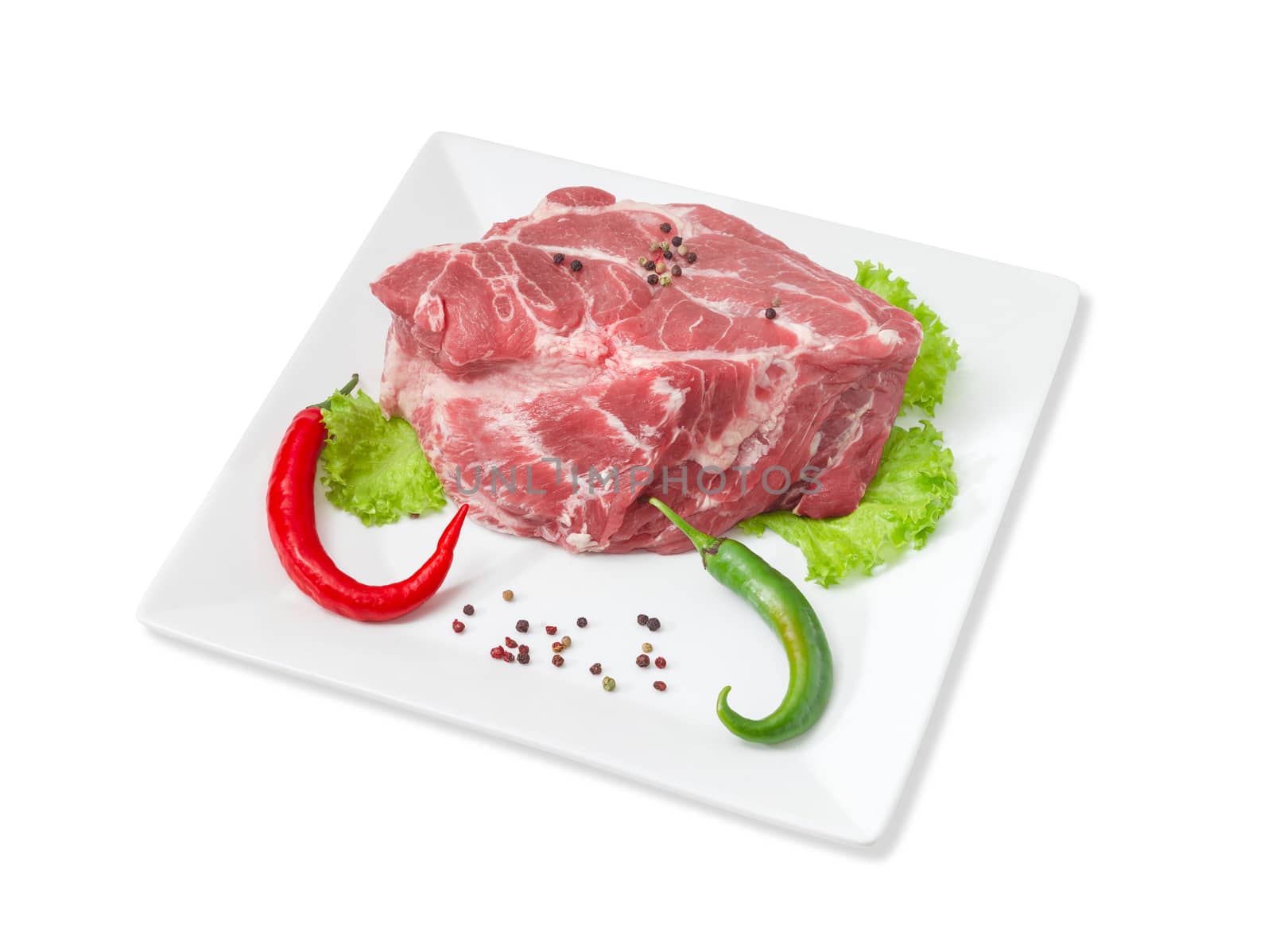 Piece of a fresh uncooked pork neck, green and red chili, black and red pepper, lettuce on a white square dish on a light background
