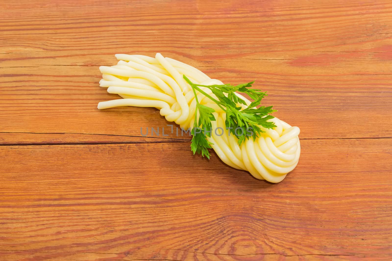 Mozzarella cheese in the shape of strings, twisted to form a plait and twig of parsley on an old wooden surface
