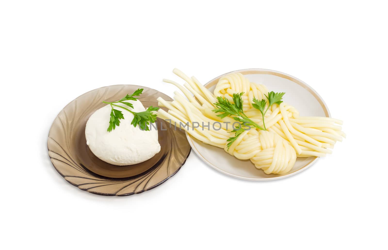 Ball of the fresh soaked mozzarella cheese on the glass saucer, two portions of the mozzarella cheese, twisted to form a plait on the other saucer and twigs of parsley on a light background
