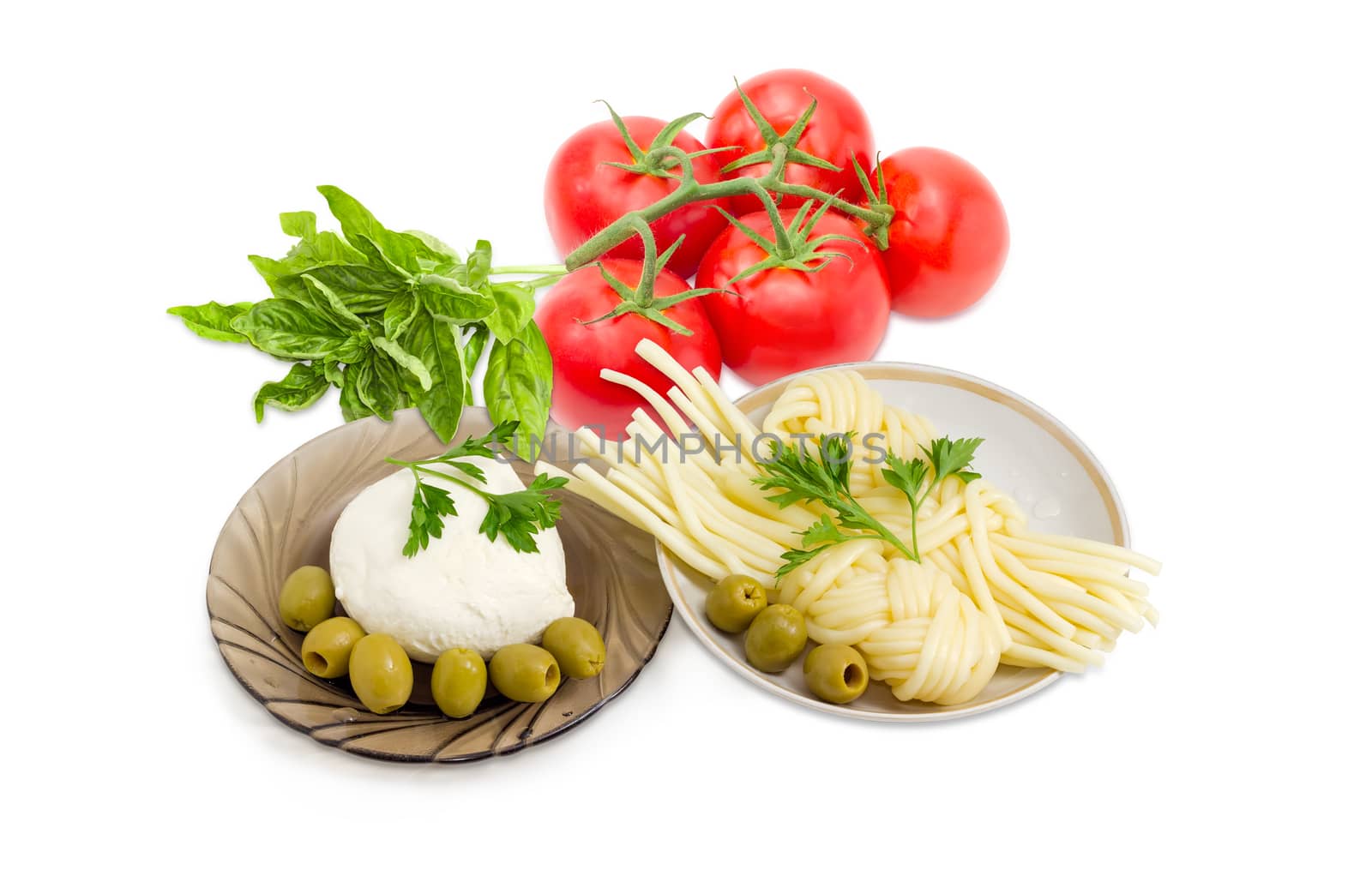 Ball of the fresh mozzarella cheese on the glass saucer, mozzarella cheese twisted to form a plait on the other saucer, green olives, tomatoes, basil and twigs of parsley on a light background
