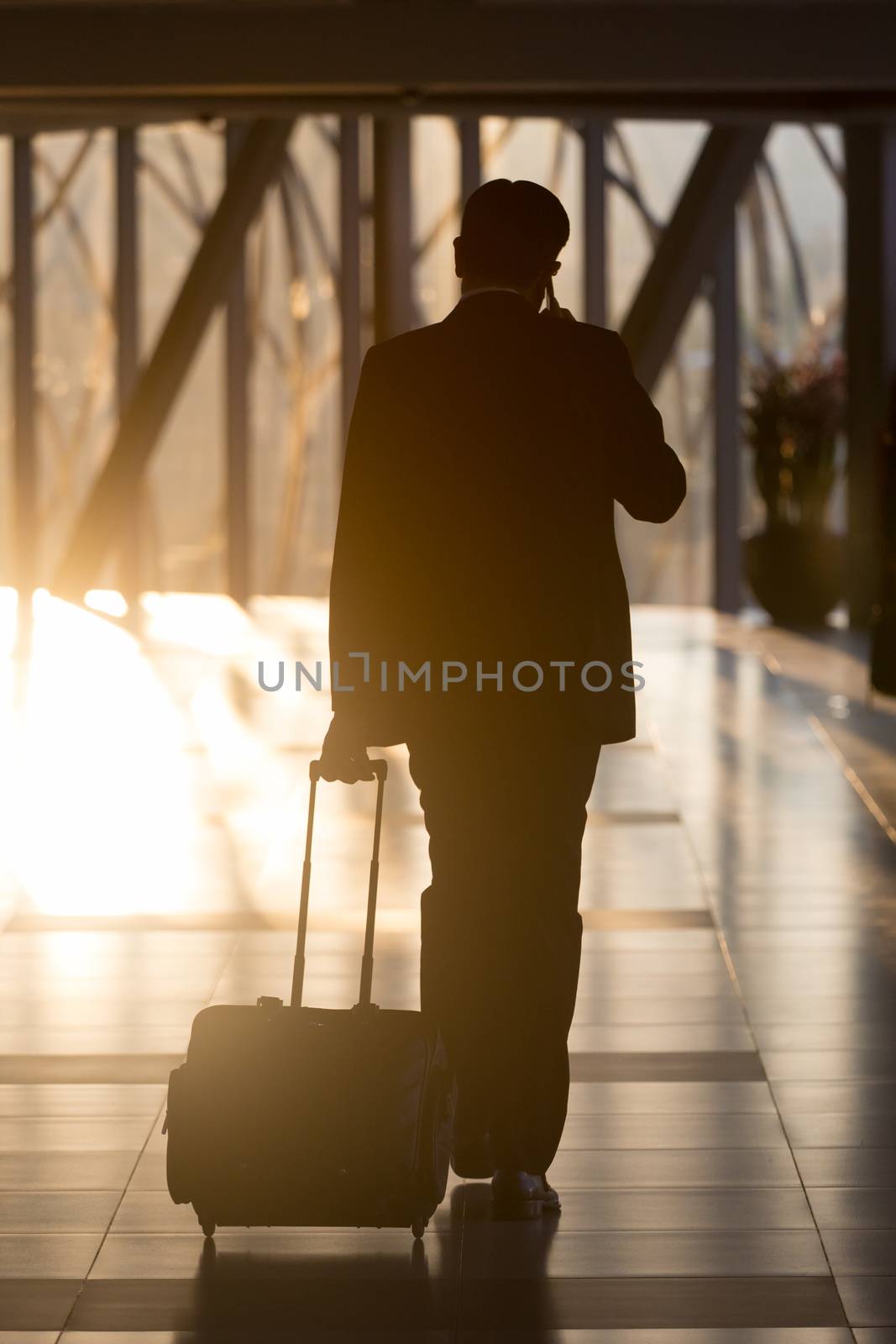Businessman dragging a small carry on luggage suitcase at airport corridor walking to departure gates.