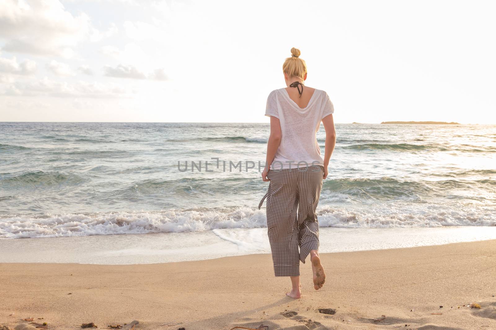 Woman walking on sand beach at golden hour. Seashore sunset walk.