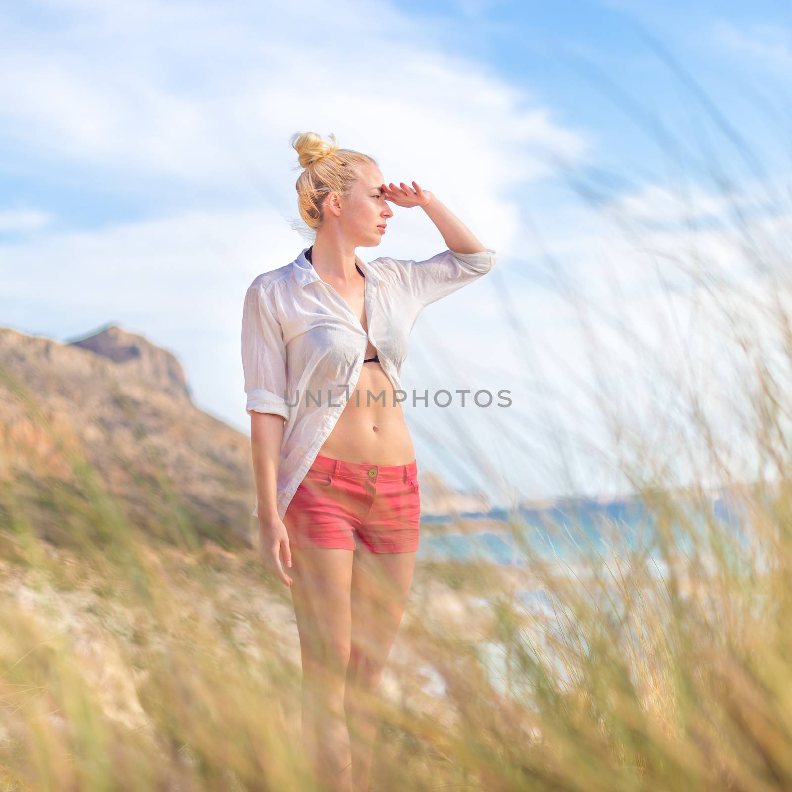 Relaxed woman in white shirt looking at distance, enjoying beautiful nature, freedom and life at serene landscape at Balos beach, Greece. Concept of vacations, freedom, happiness, joy and well being.