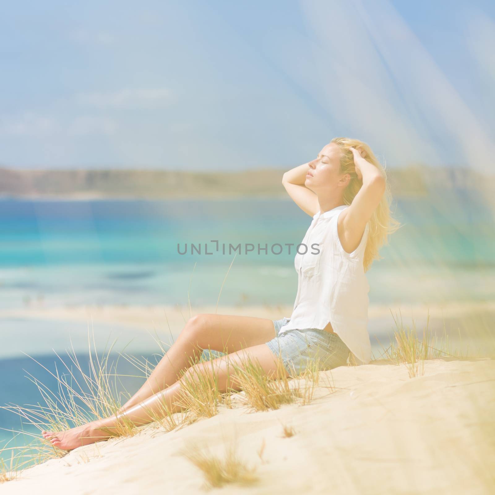 Relaxed woman enjoying sun, freedom and life an a beautiful sandy beach of Balos in Greece. Young lady feeling free, relaxed and happy. Vacations, freedom, happiness, enjoyment and well being.