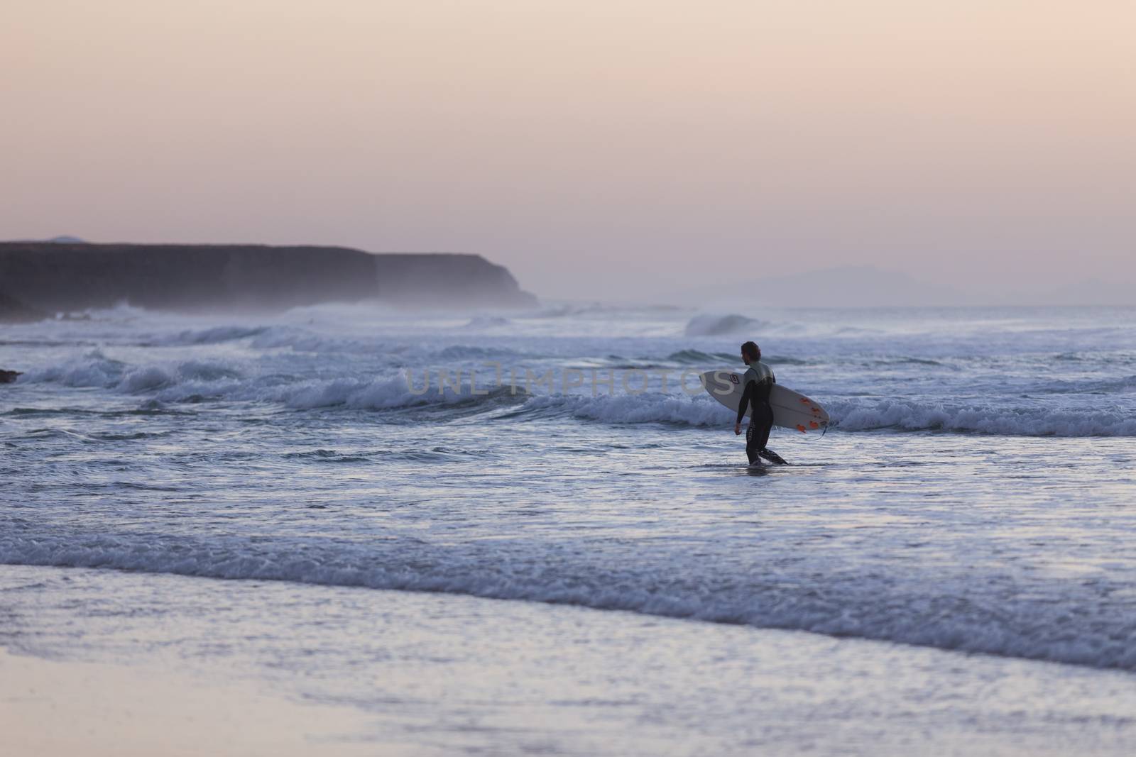 Male surfers on beach with surfboard at dusk at El Cotillo beach, famous surfing destination on Fuerteventura, Canary Islands, Spain. Panoramic composition.