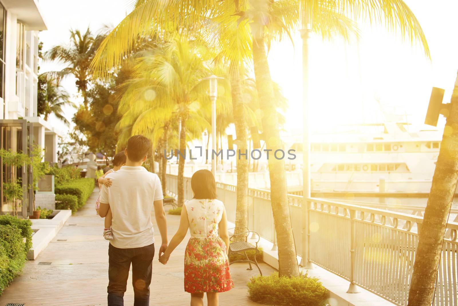 Rear view of Asian family enjoying outdoor activity together, walking in beautiful sunset during holiday vacation, outside the resort.