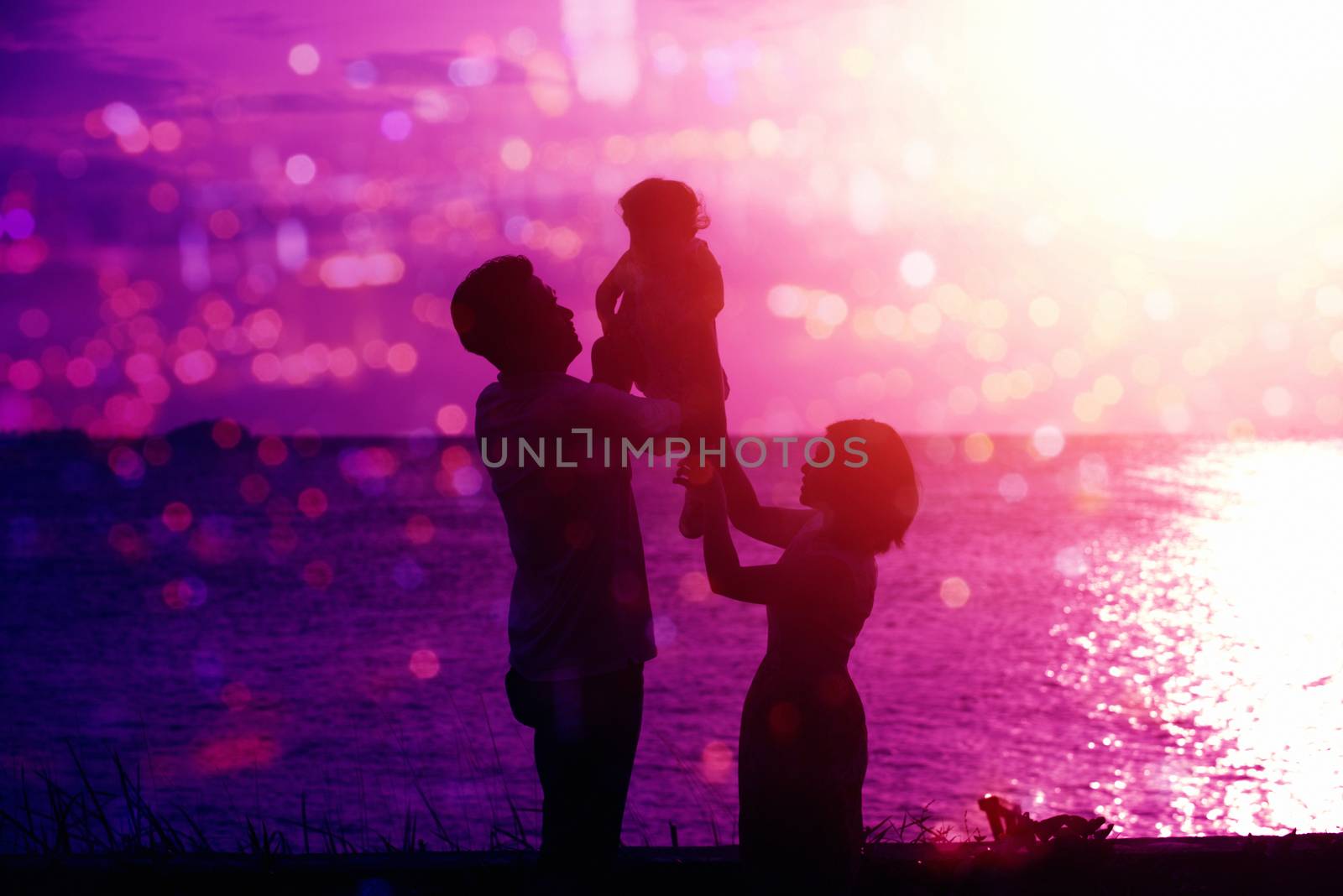 Silhouette of happy family enjoying outdoor activity together, standing on coastline in beautiful sunset during holiday vacations.